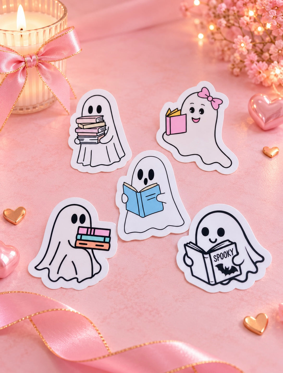 Five cute ghost-shaped stickers with different Halloween-themed illustrations are arranged on a pink background with a candle, ribbon, and small hearts.