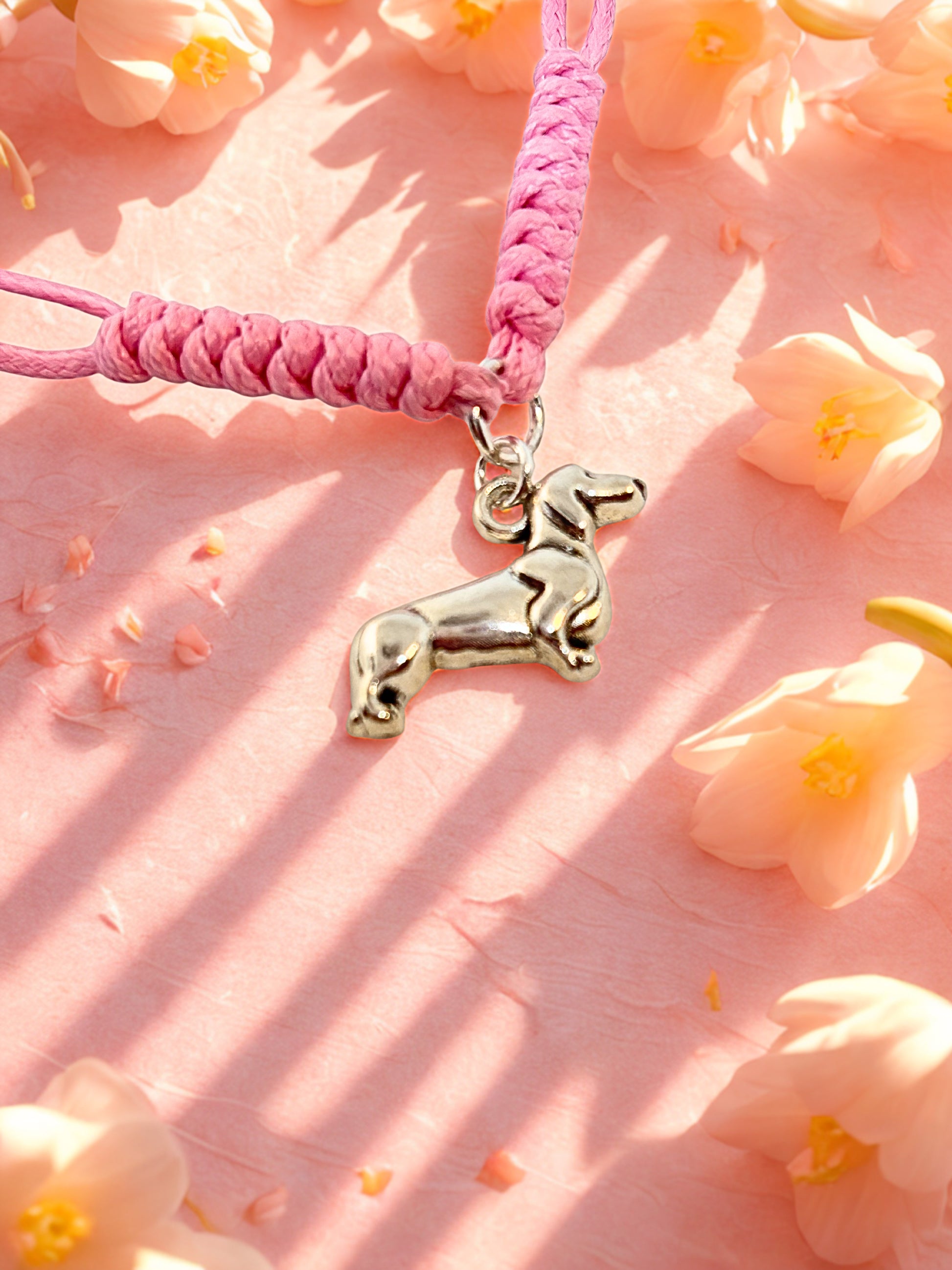 Pink cord bracelet with a silver dog charm on a pink floral background