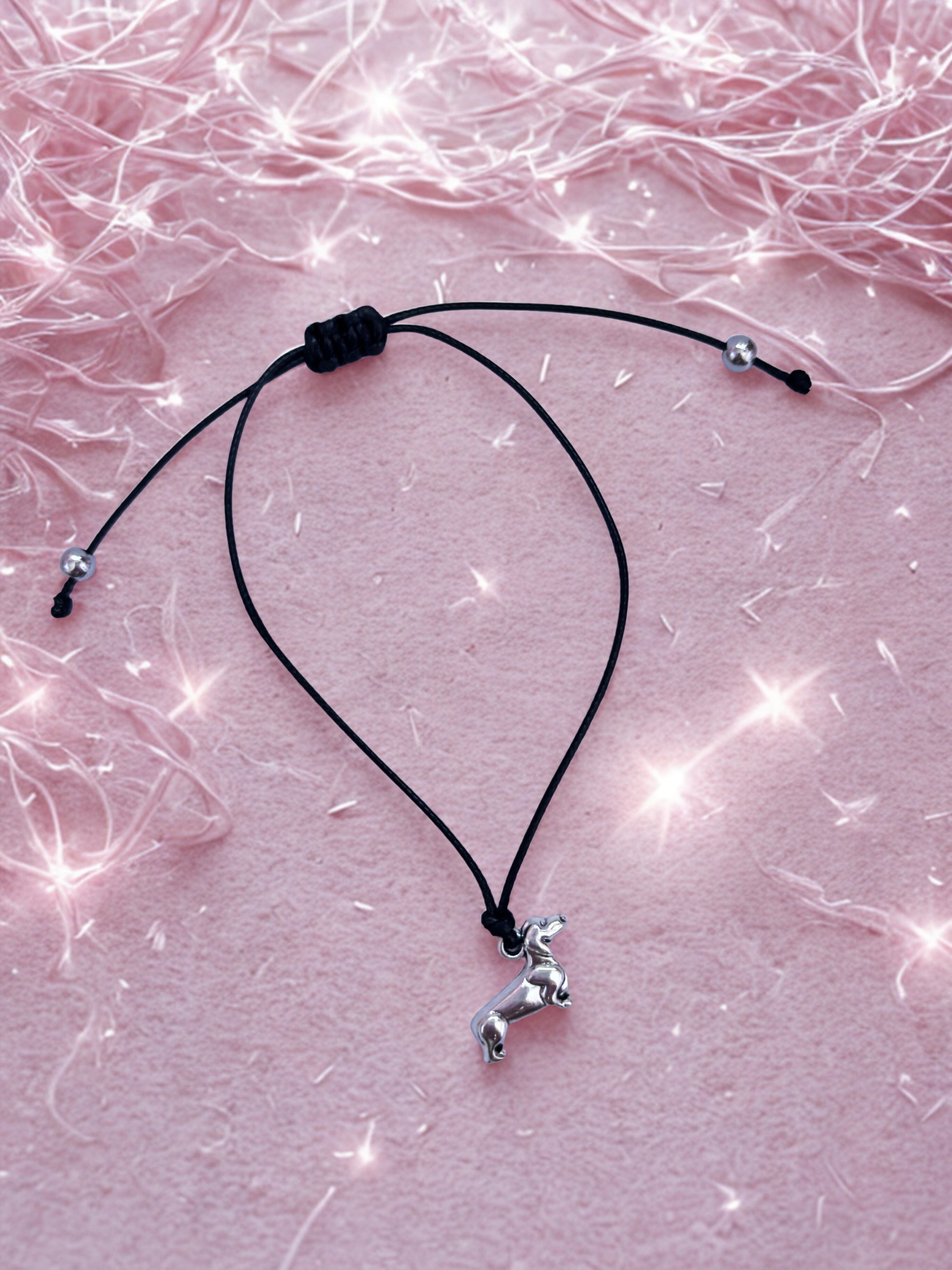 Black cord bracelet  with a small silver dachshund dog pendant on a pink textured background