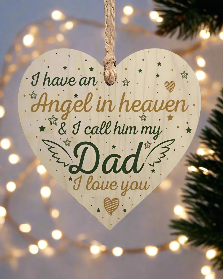 Heart-shaped wooden plaque with text 'I have an Angel in heaven & I call him my Dad I love you' on a Christmas tree with lights.