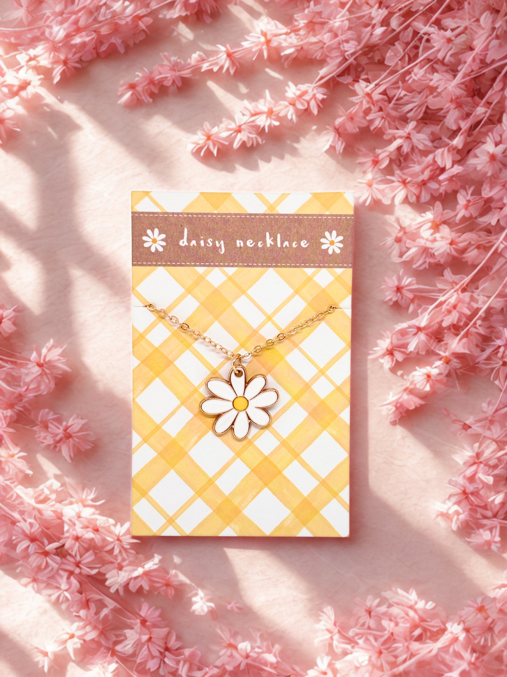 Daisy necklace on a yellow and white patterned card with pink flowers around