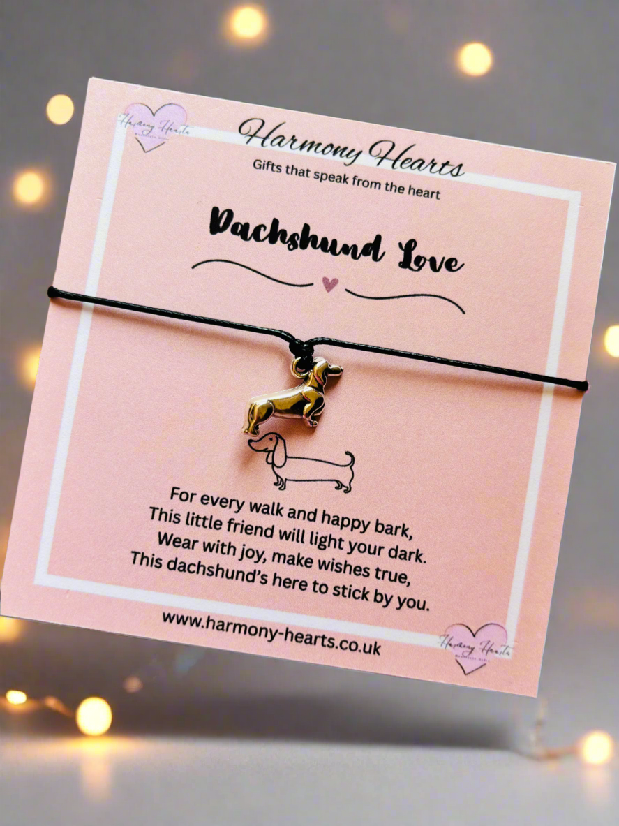 Dachshund-themed bracelet on a pink card with text, against a blurred background with lights.