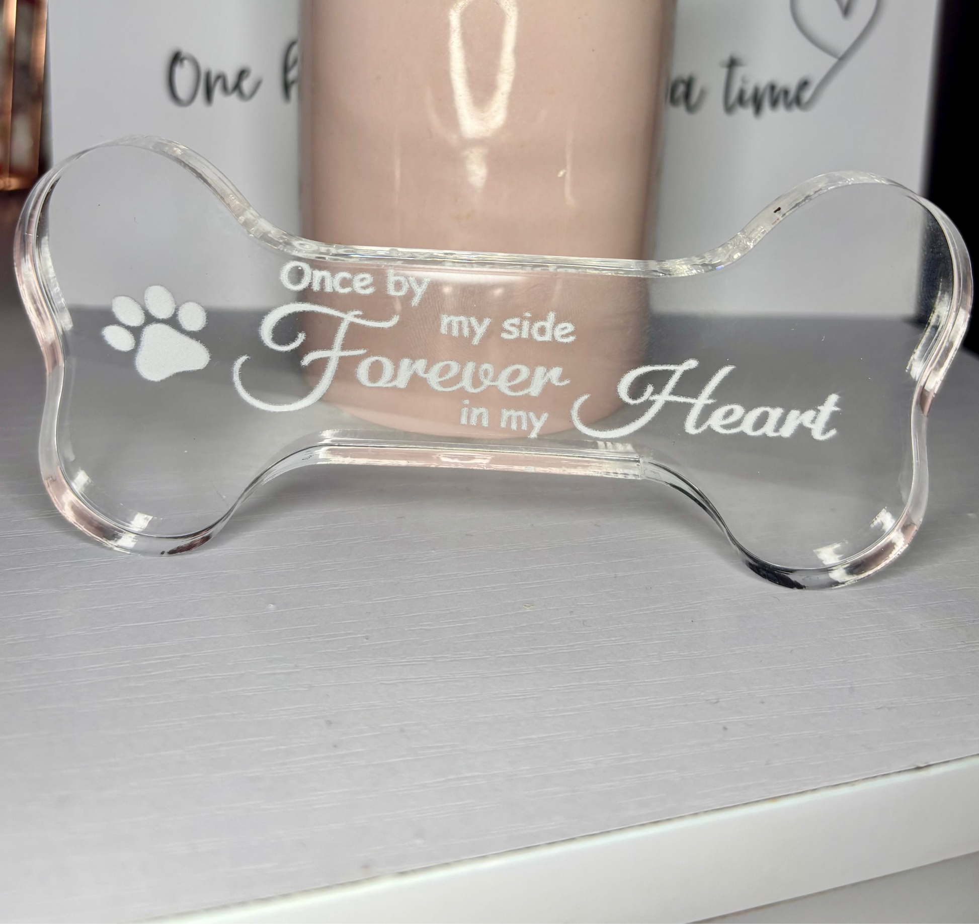 Clear acrylic pet memorial bone with engraved text on a gray surface
