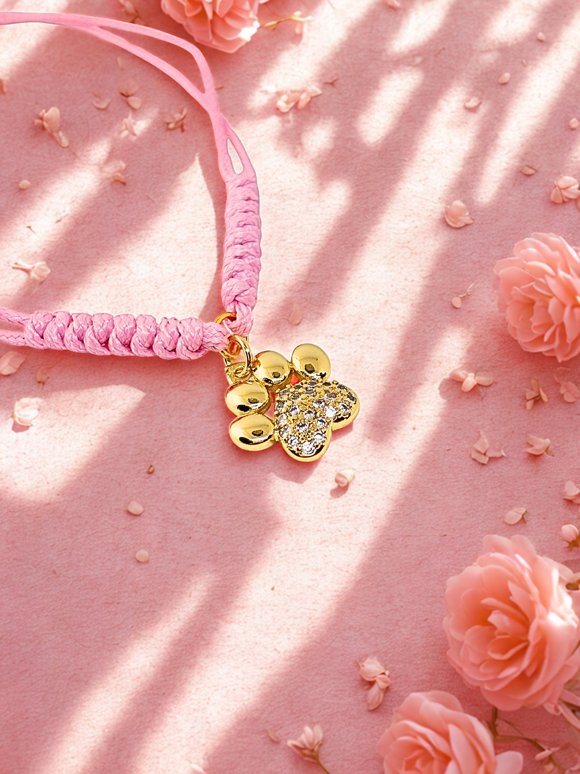 Pink cord bracelet with gold paw charm on a pink floral background