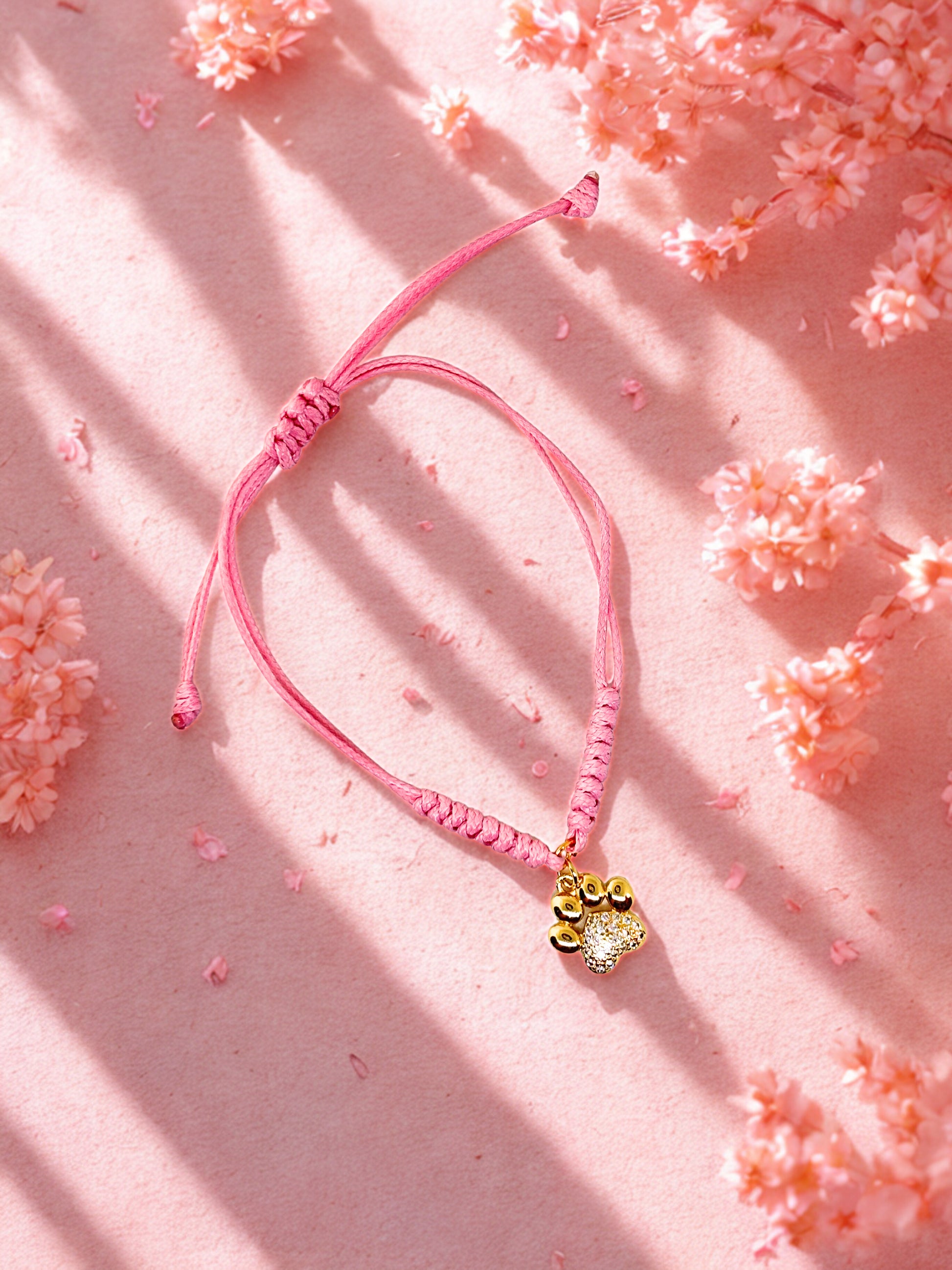 Pink bracelet with a gold paw print charm on a pink floral background