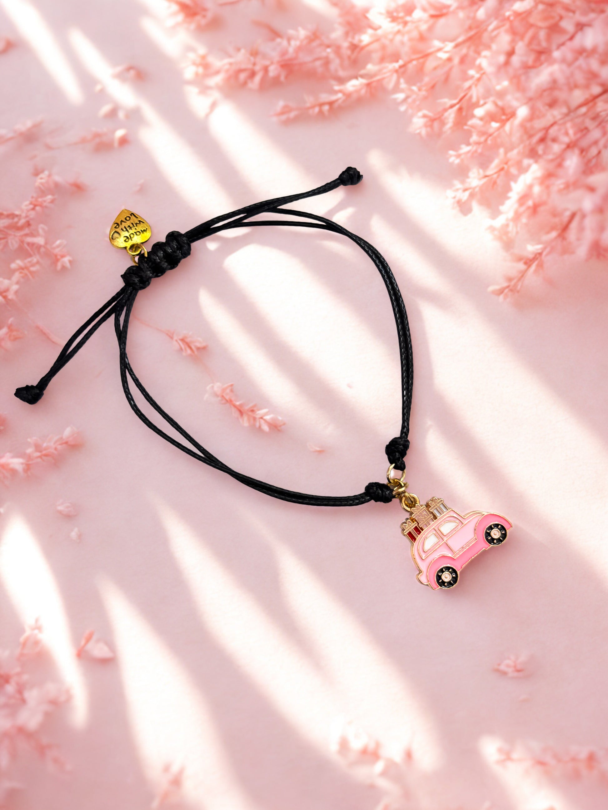 Black cord bracelet with pink car charm on a pink background