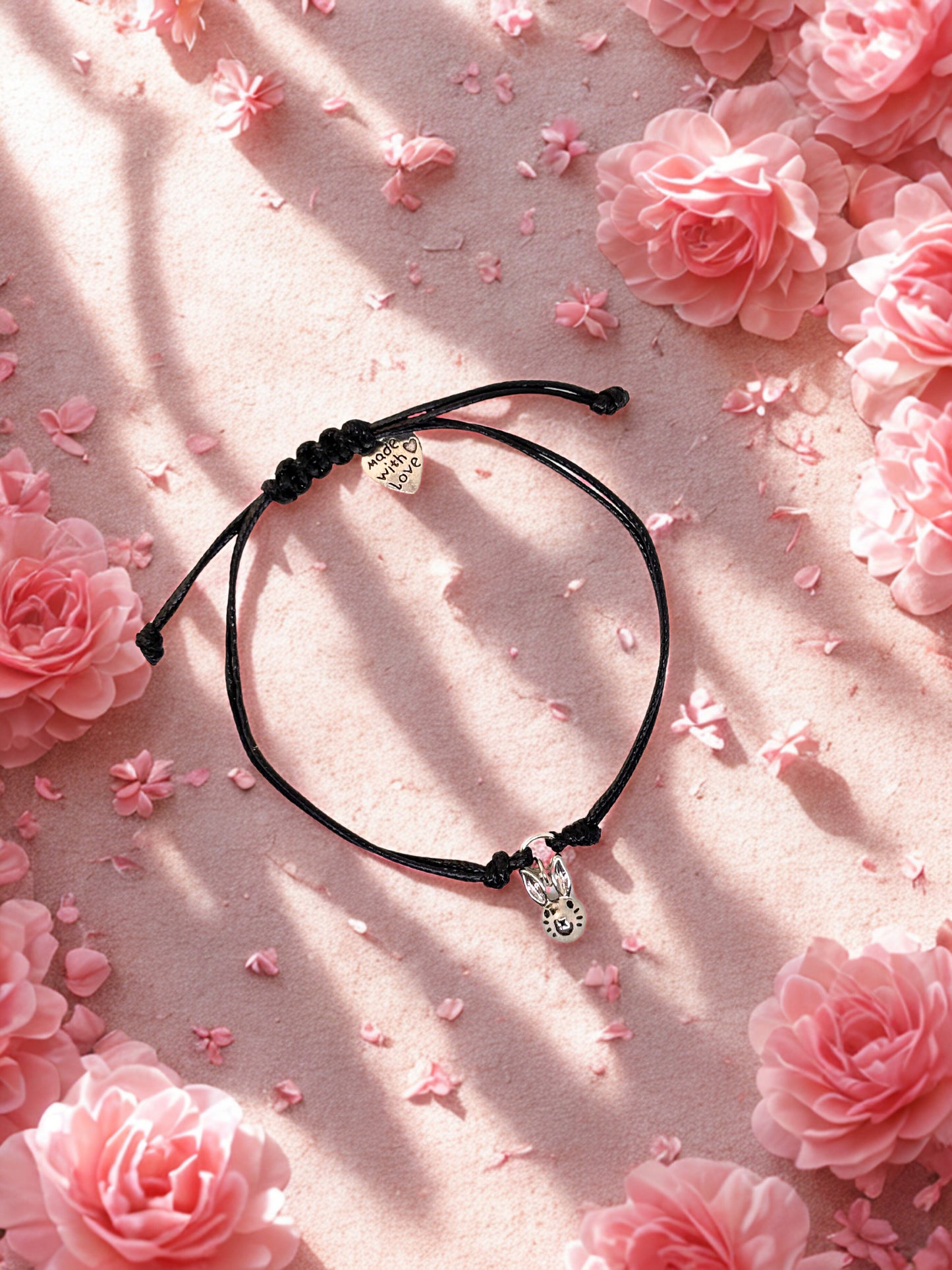 Black cord bracelet with silver bunny  charm on a pink floral background