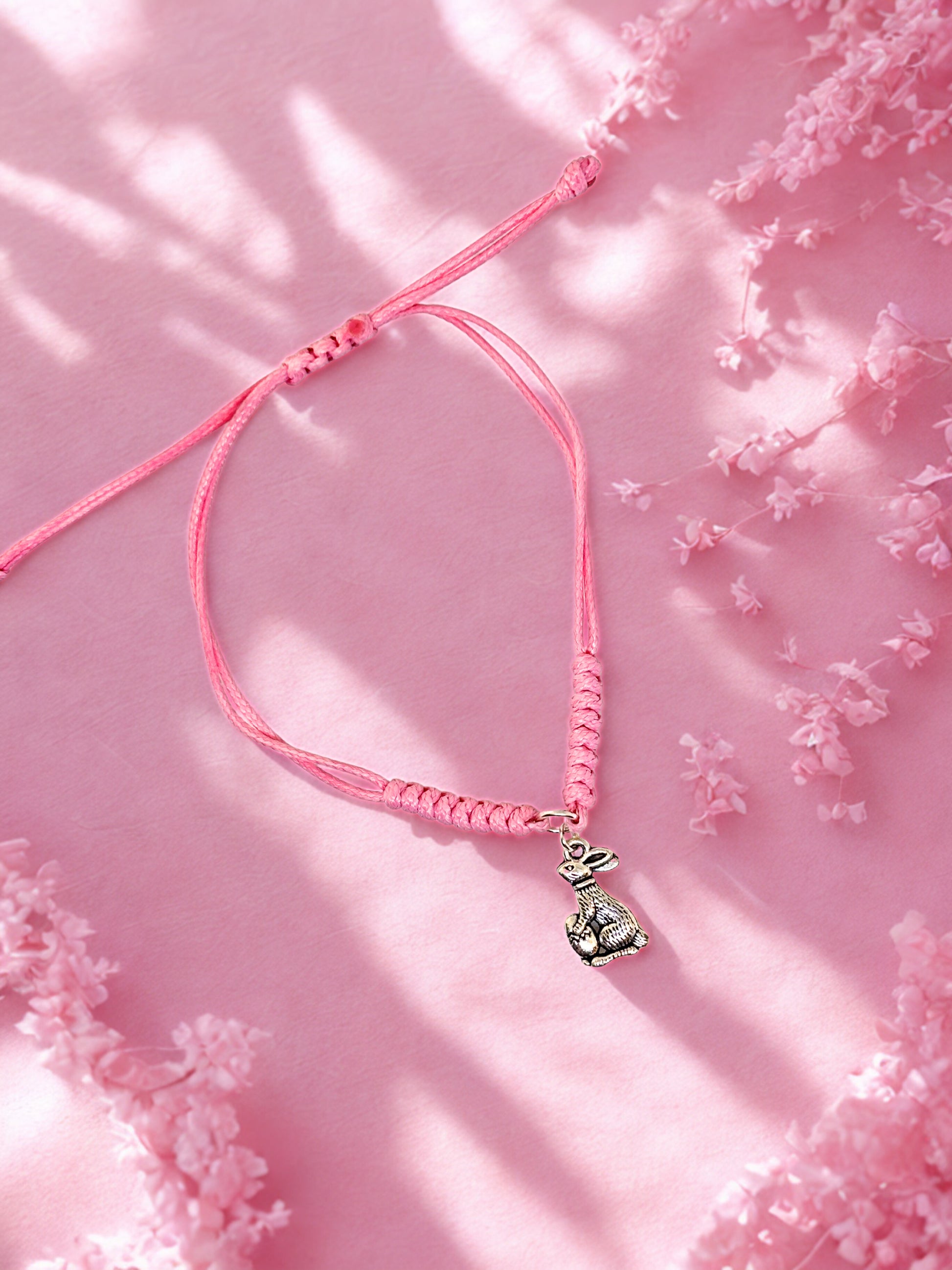 Pink braided bracelet with a silver bunny charm on a pink floral background