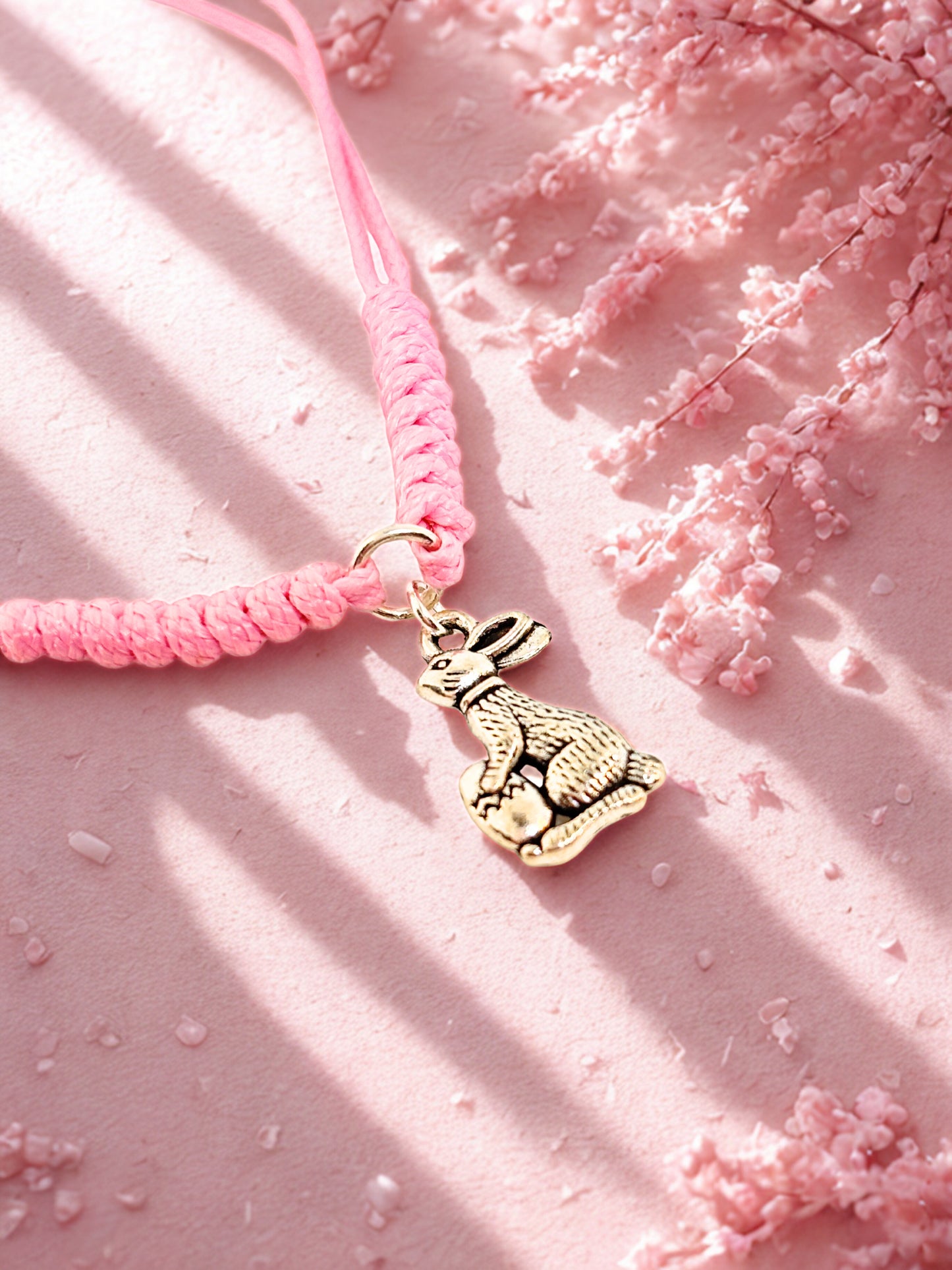 Pink cord bracelet with a silver bunny charm on a pink textured background