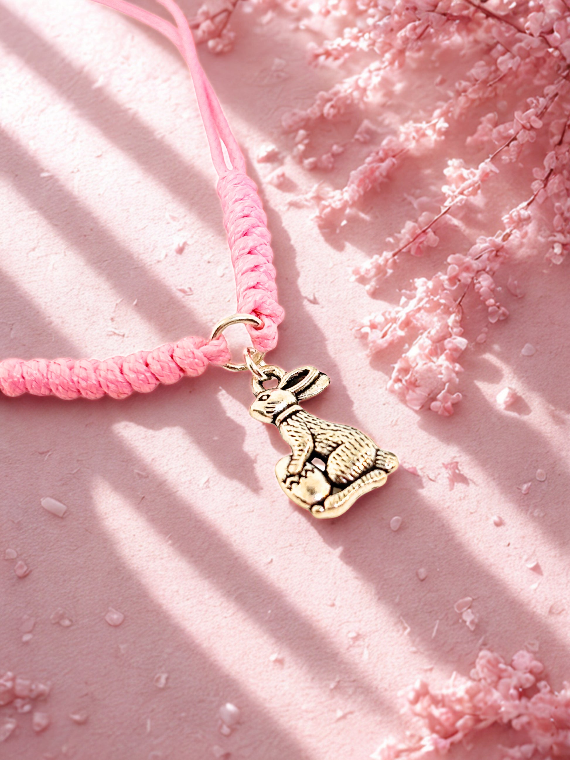 Pink cord bracelet with a silver bunny charm on a pink textured background