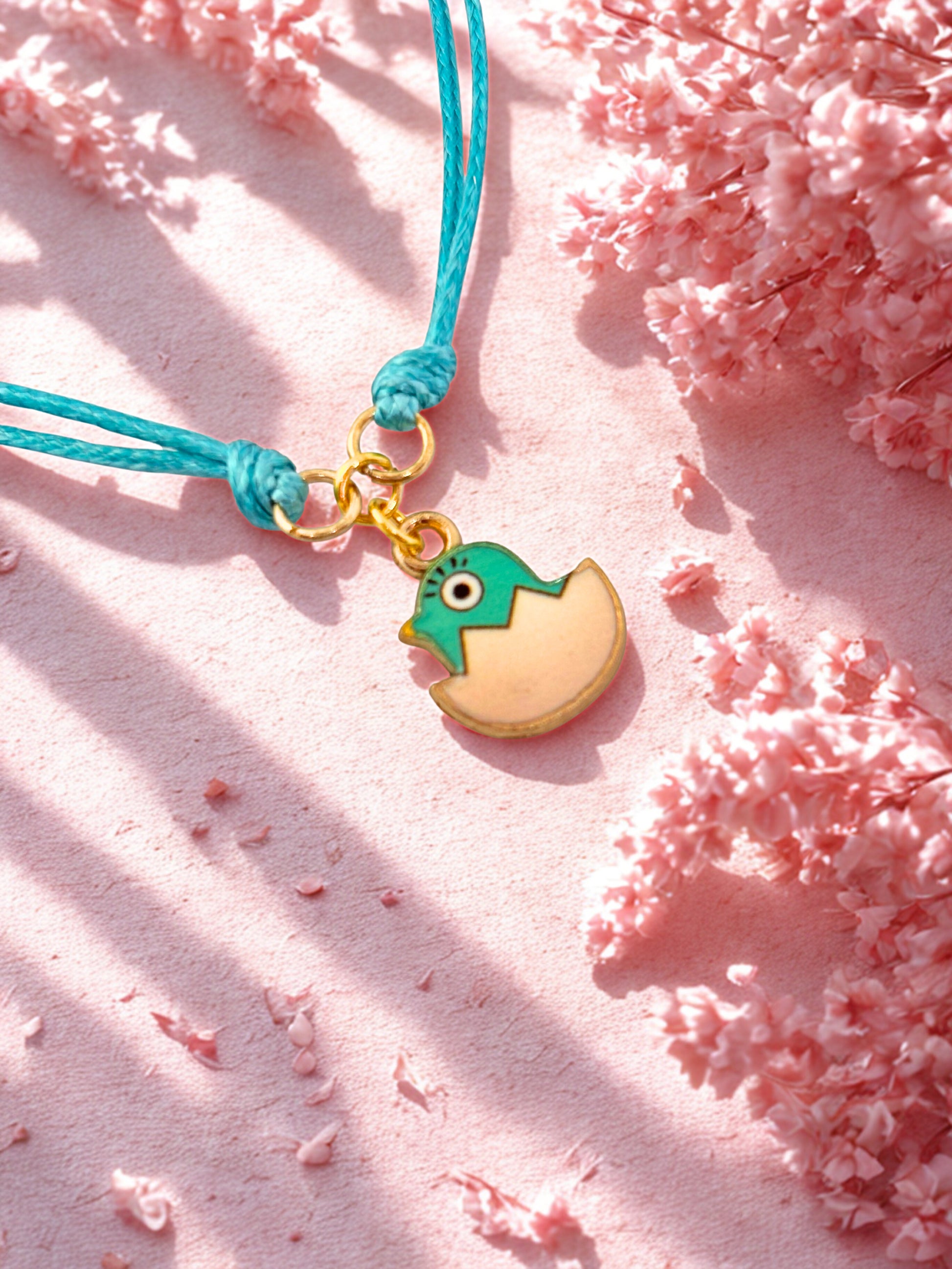 Bracelet with an Easter chick charm on a pink surface with cherry blossoms