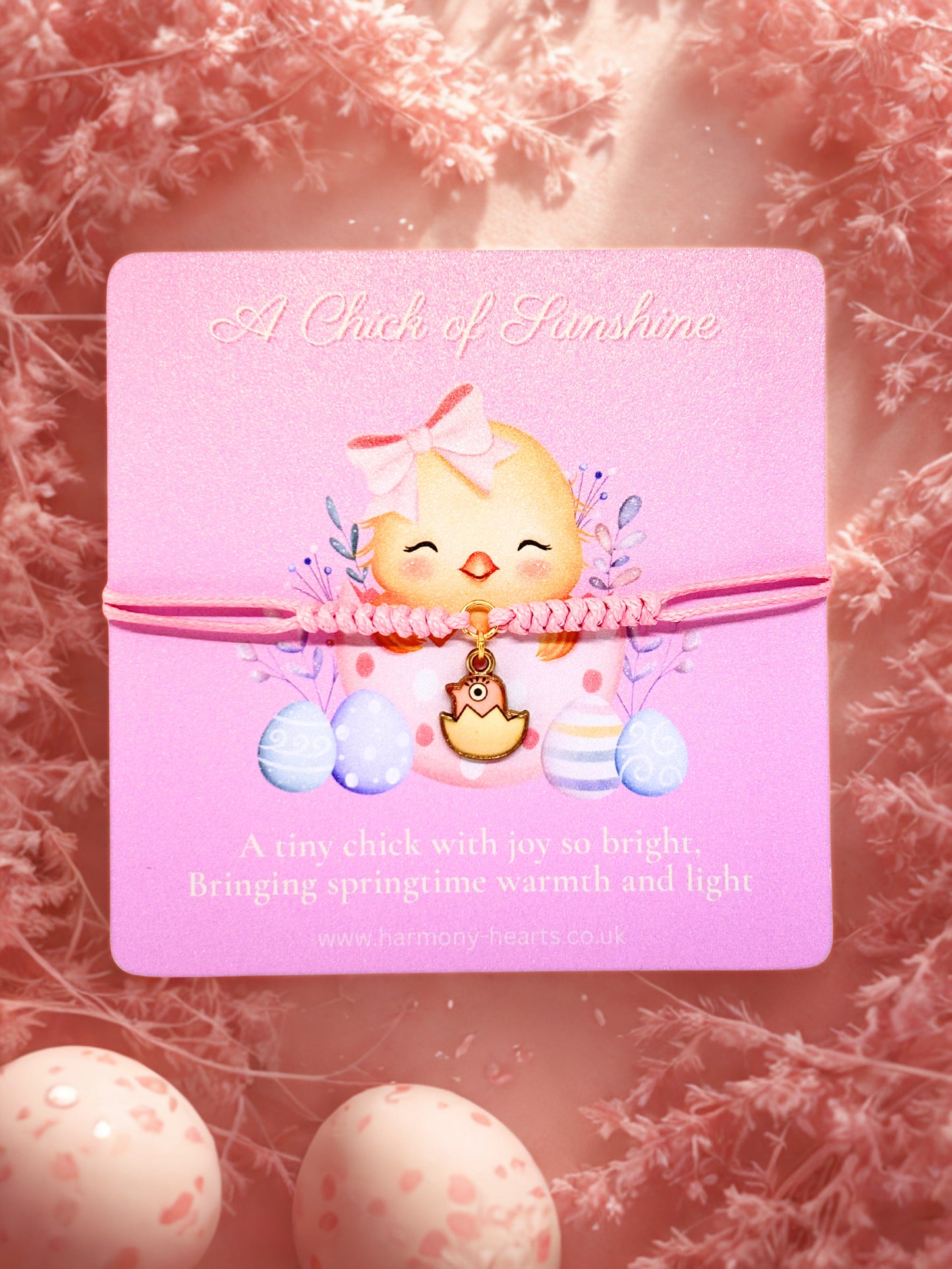 Pink card with a chick illustration and text with a cute chick charm bracelet on a soft pink floral background