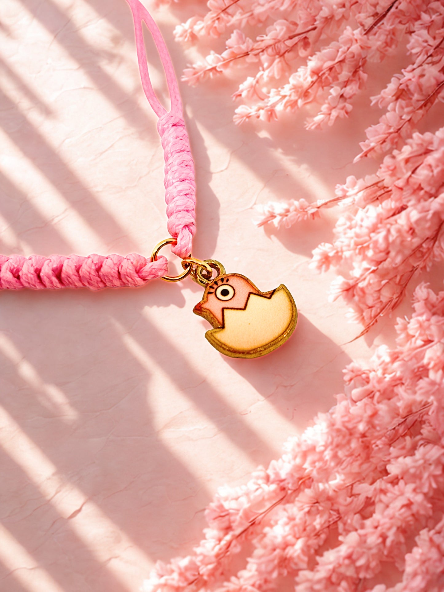 Pink cord bracelet with a pink chick charm on a pink floral background