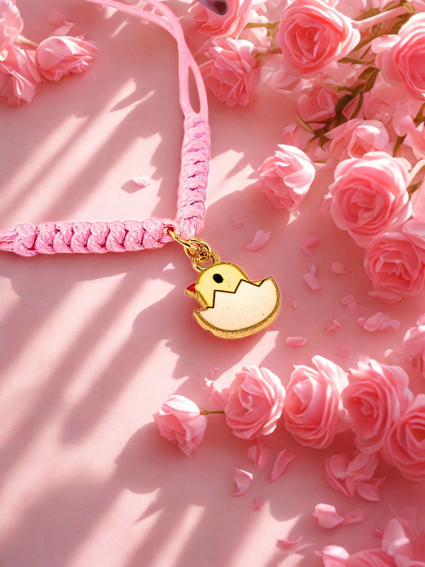 Pink braided bracelet with a yellow chick charm on a pink floral background