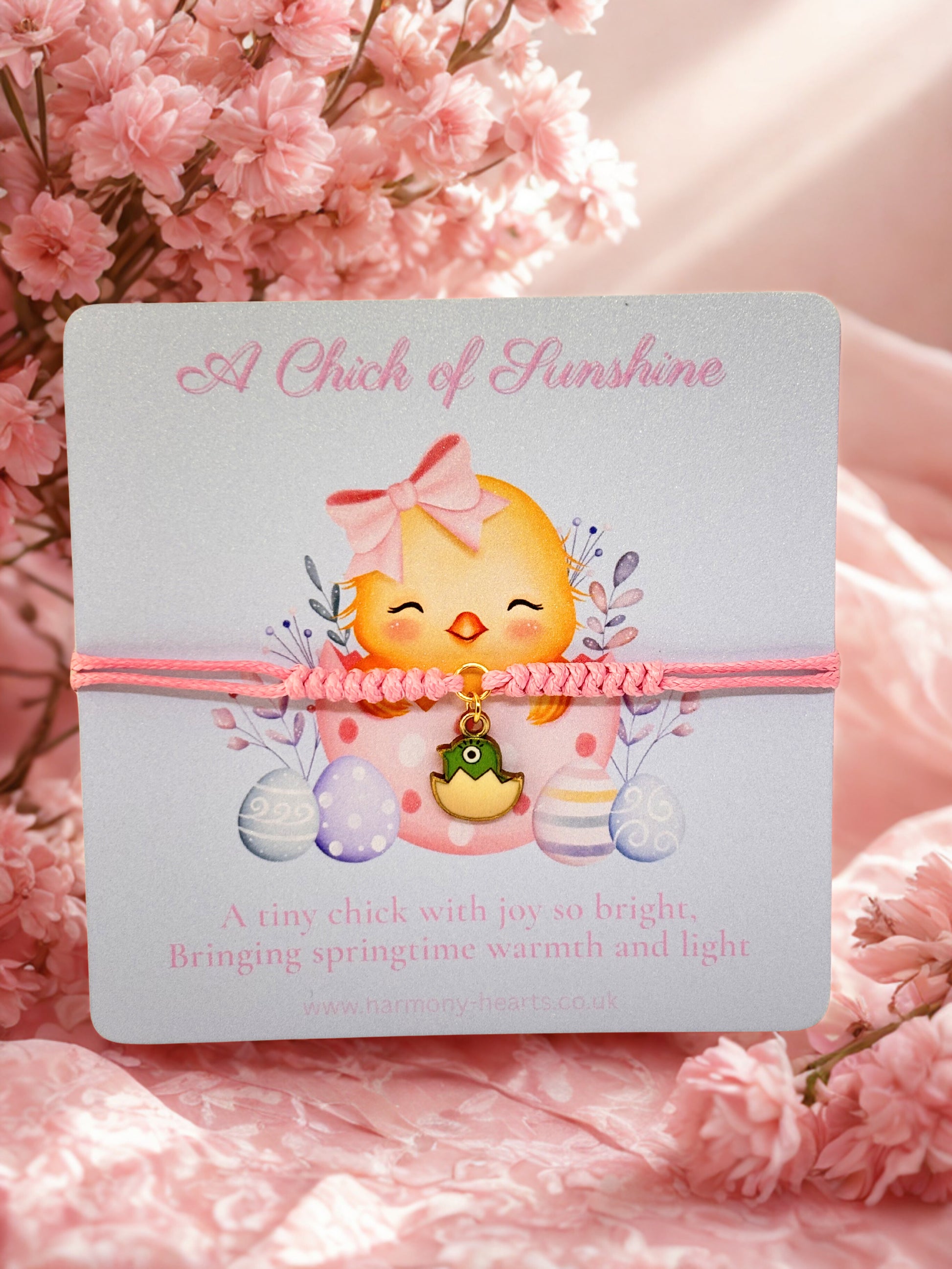 Pink cord bracelet with a chick charm on a branded Harmony Hearts Eater card with pink flowers in the background