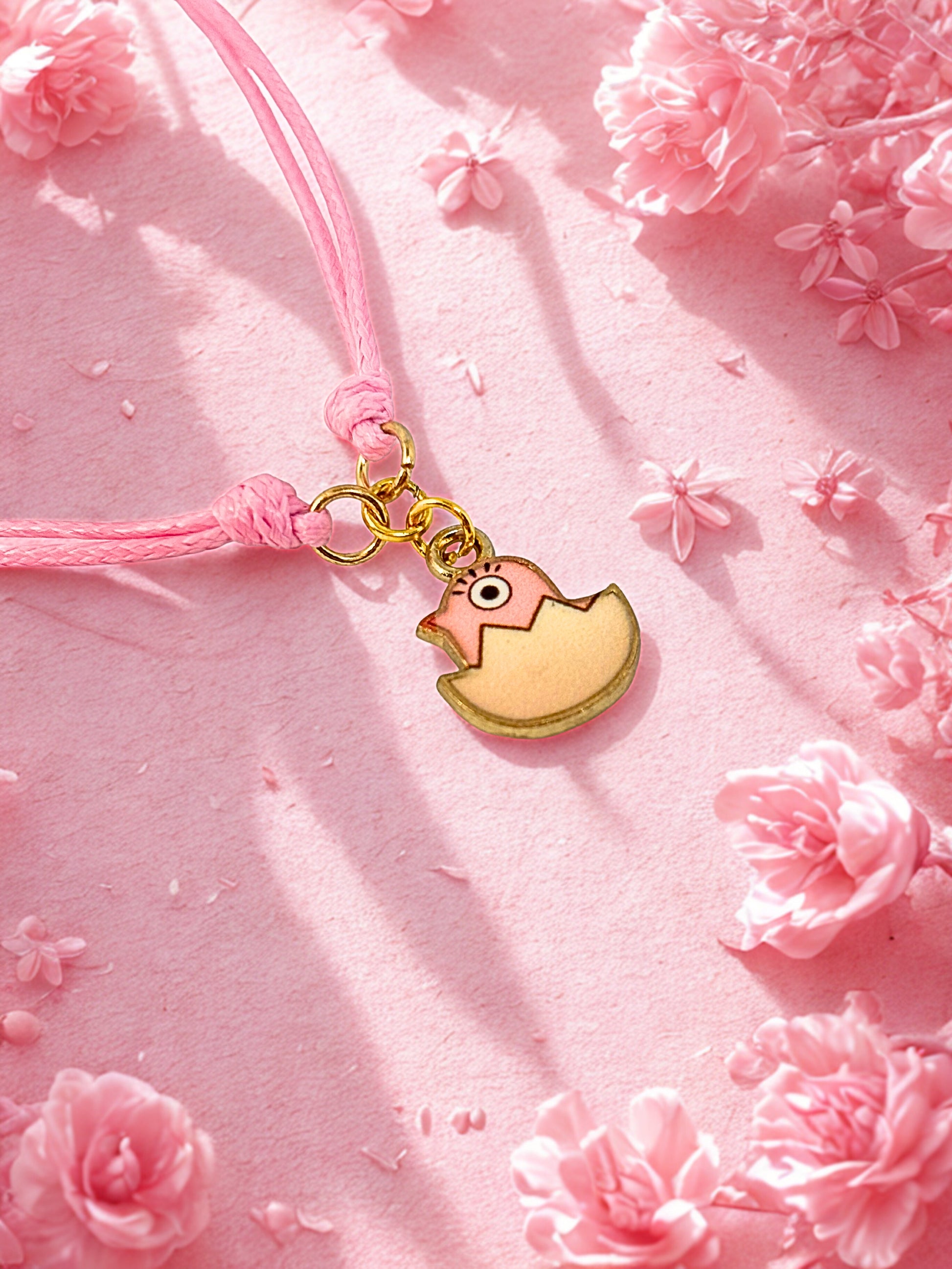 Pink Easter chick charm on a pink string with pink flowers in the background