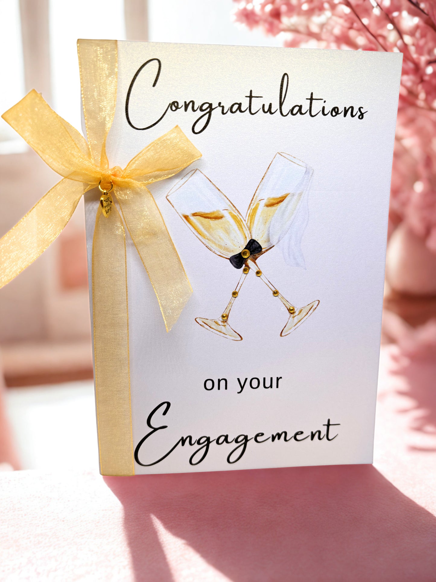 Engagement greeting card with champagne glasses and a gold bow on a blurred background