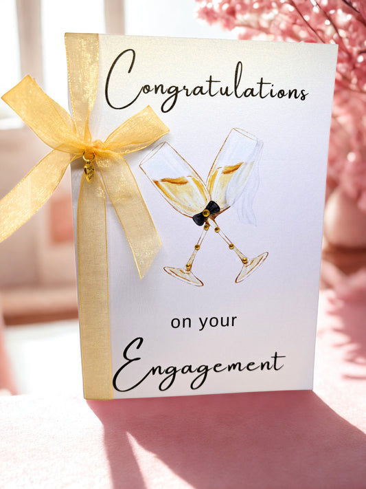 Engagement greeting card with champagne glasses and a gold bow on a blurred background