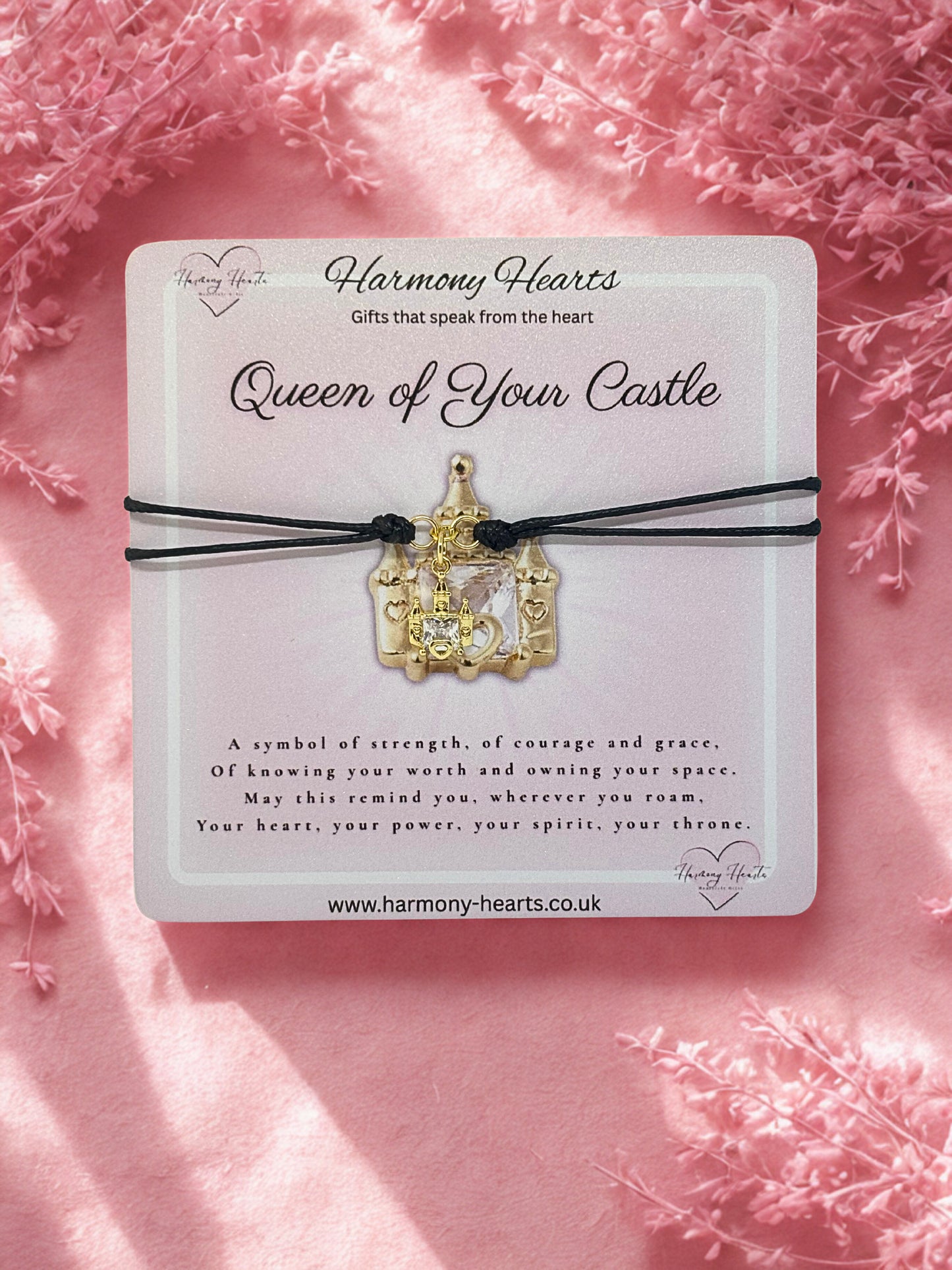 Gold castle bracelet on a pink card with decorative text and website URL, set against a soft pink floral background.