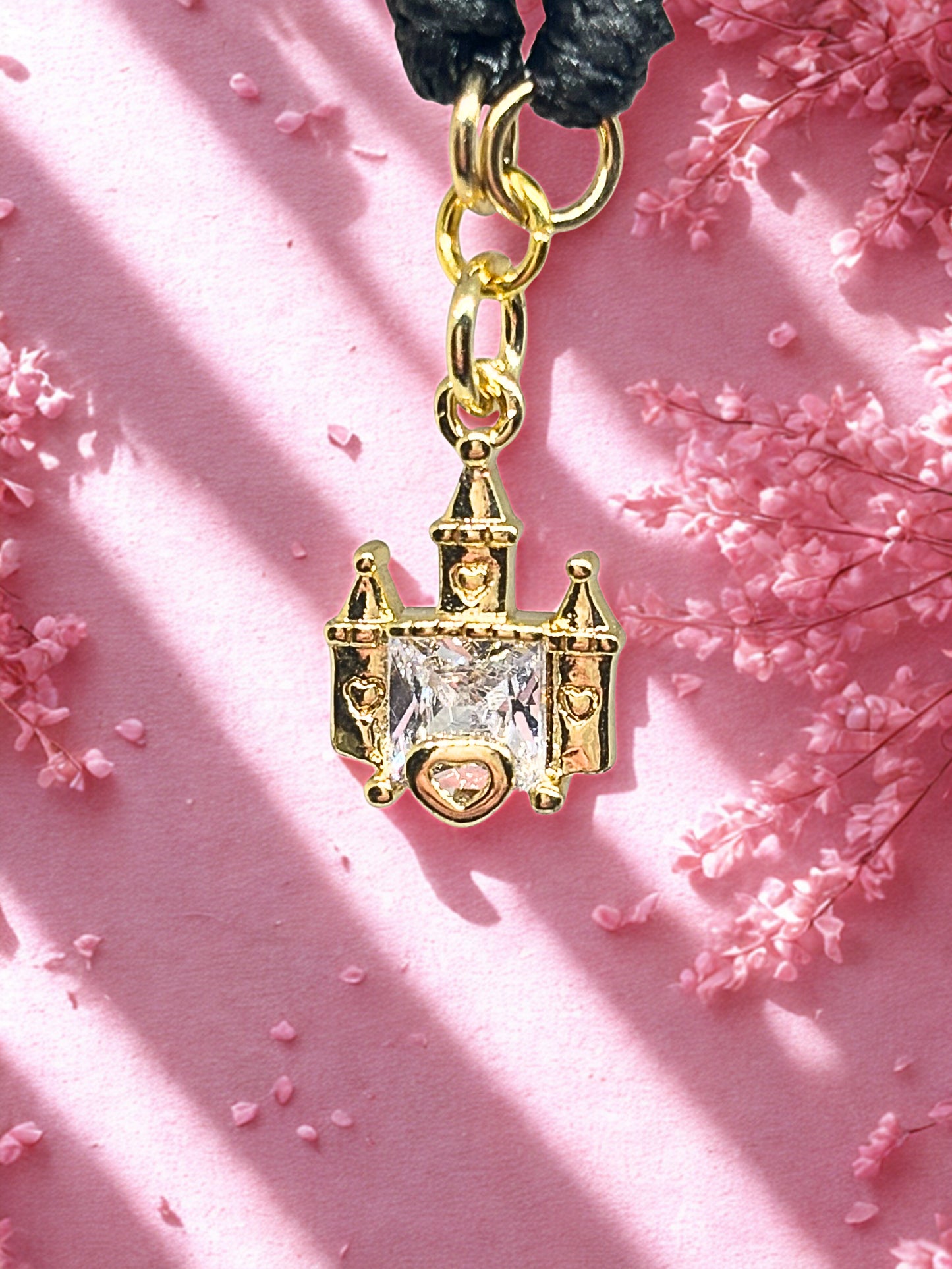 Gold castle-shaped charm with a clear gemstone on a pink background with flowers.