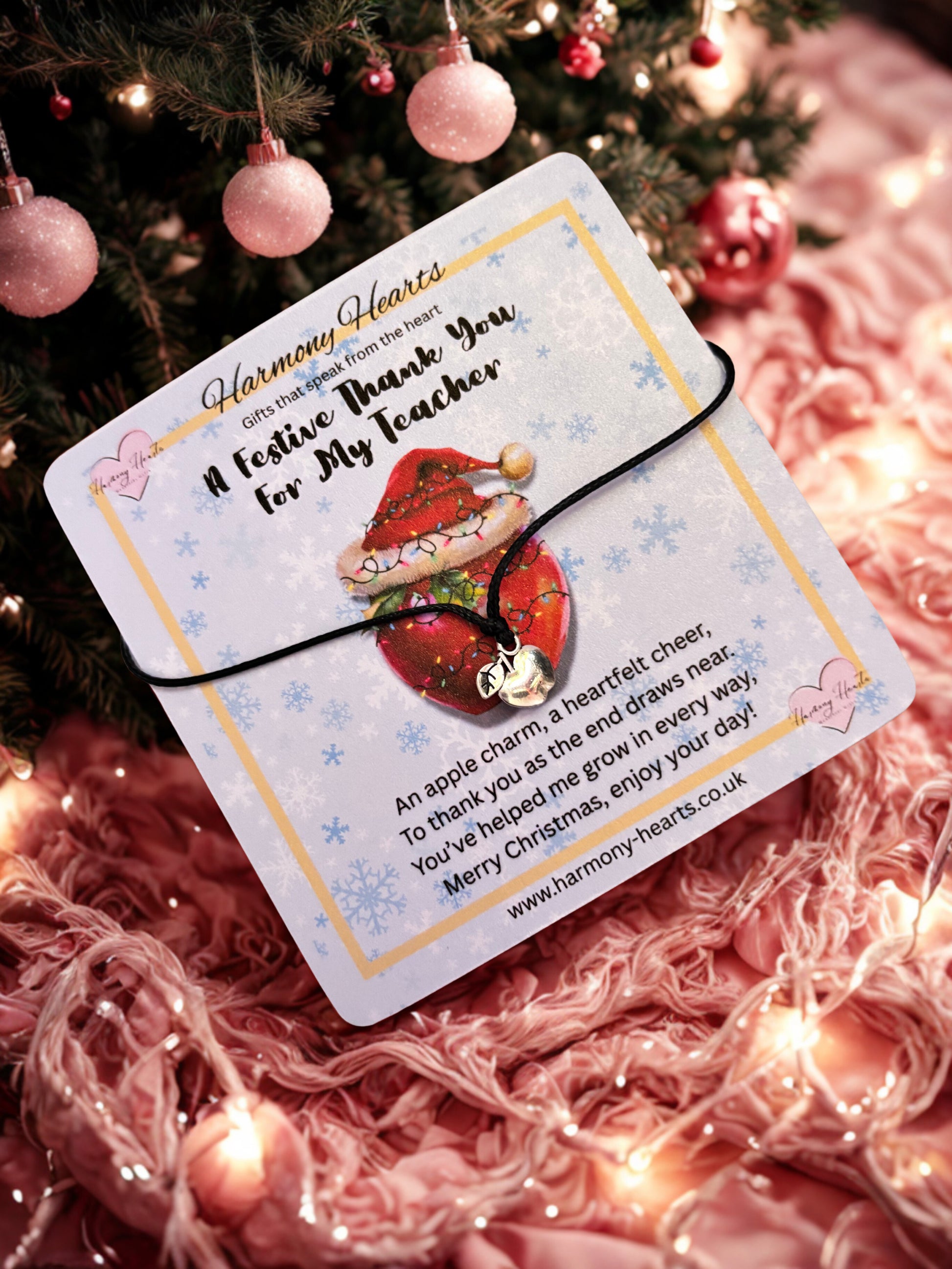 Card with an apple charm bracelet and festive design on a pink textured background with Christmas decorations.