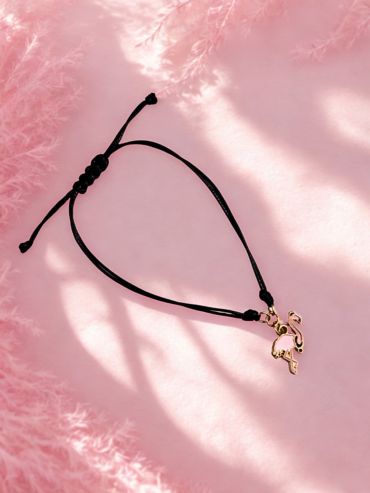 Black cord bracelet with a flamingo charm on a pink textured background