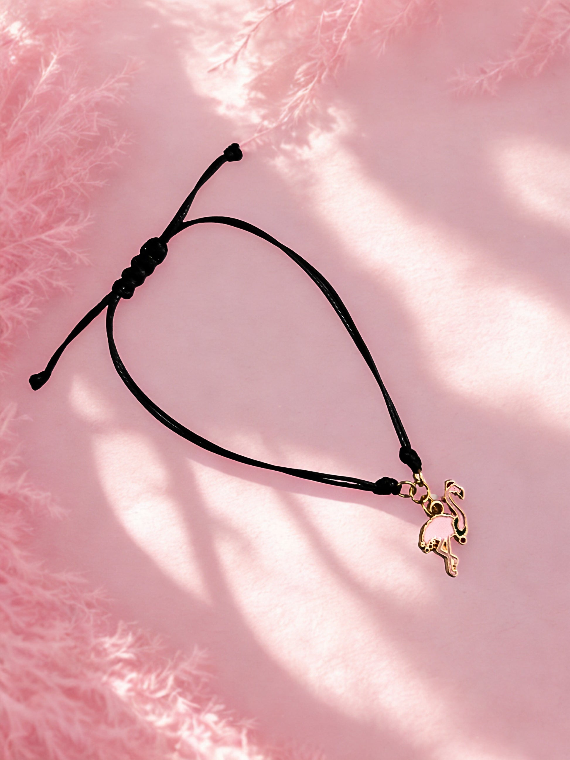 Black cord bracelet with a flamingo charm on a pink textured background