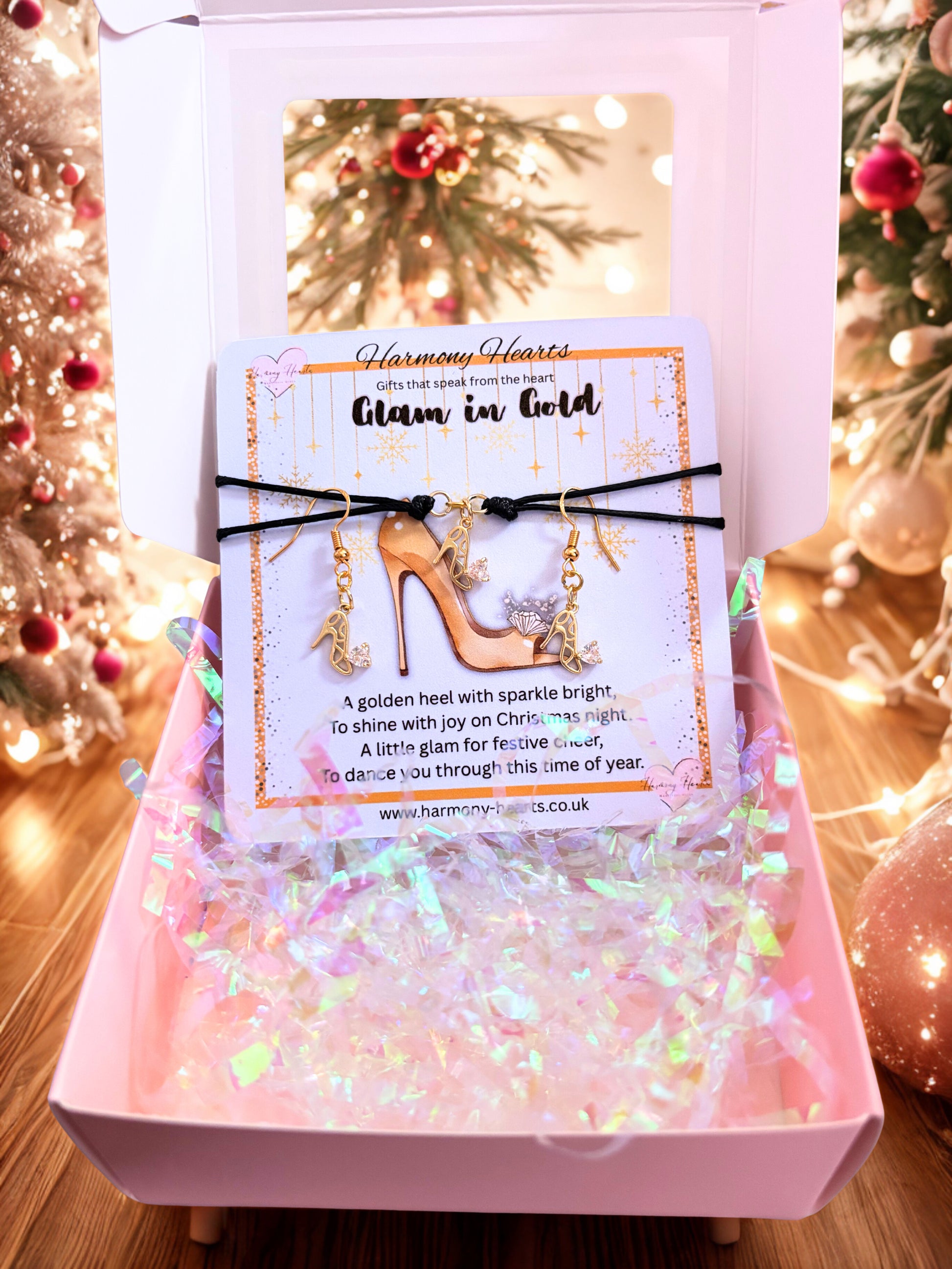 Gold high-heeled shoe charm with decorative card in a pink box against a festive background.