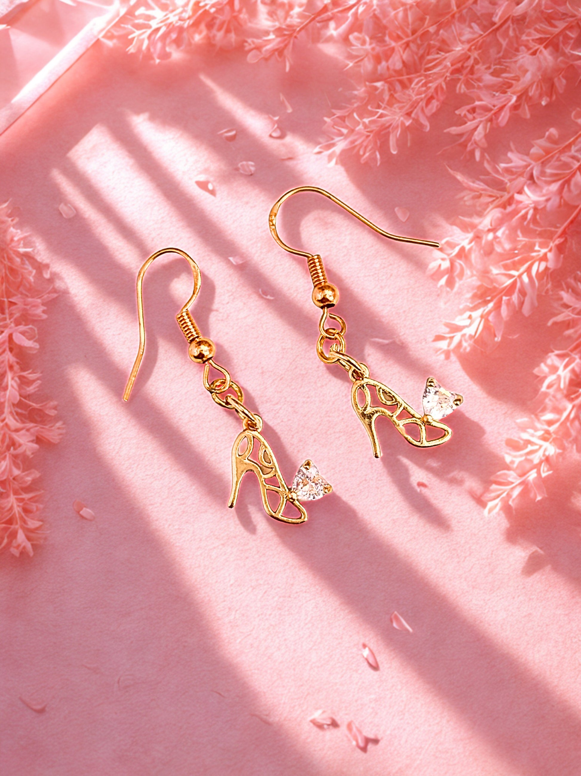 Gold high-heeled shoe earrings on a pink floral background