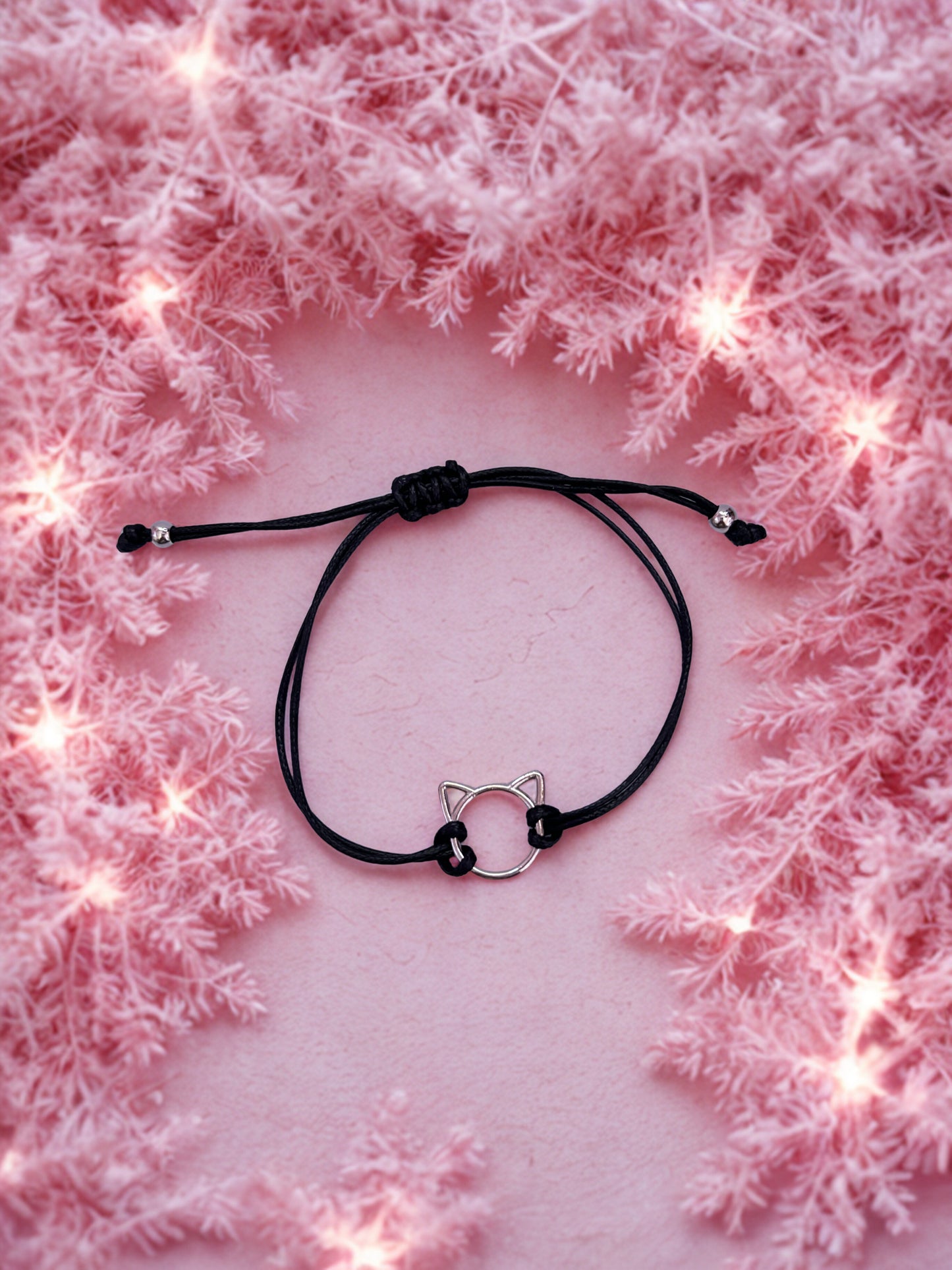 Black cord bracelet with cat ear charm on a pink textured background