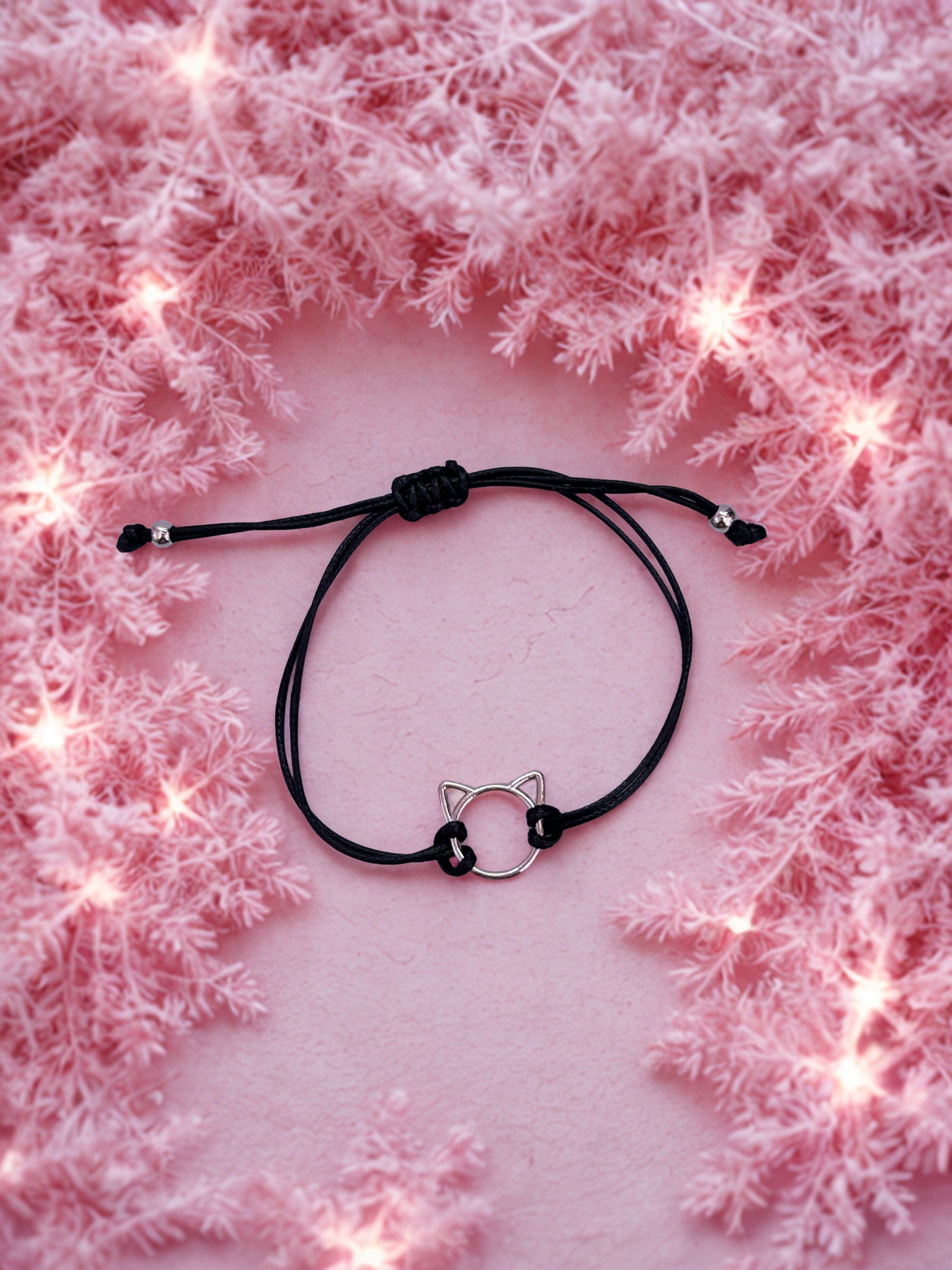 Black cord bracelet with cat ear charm on a pink textured background