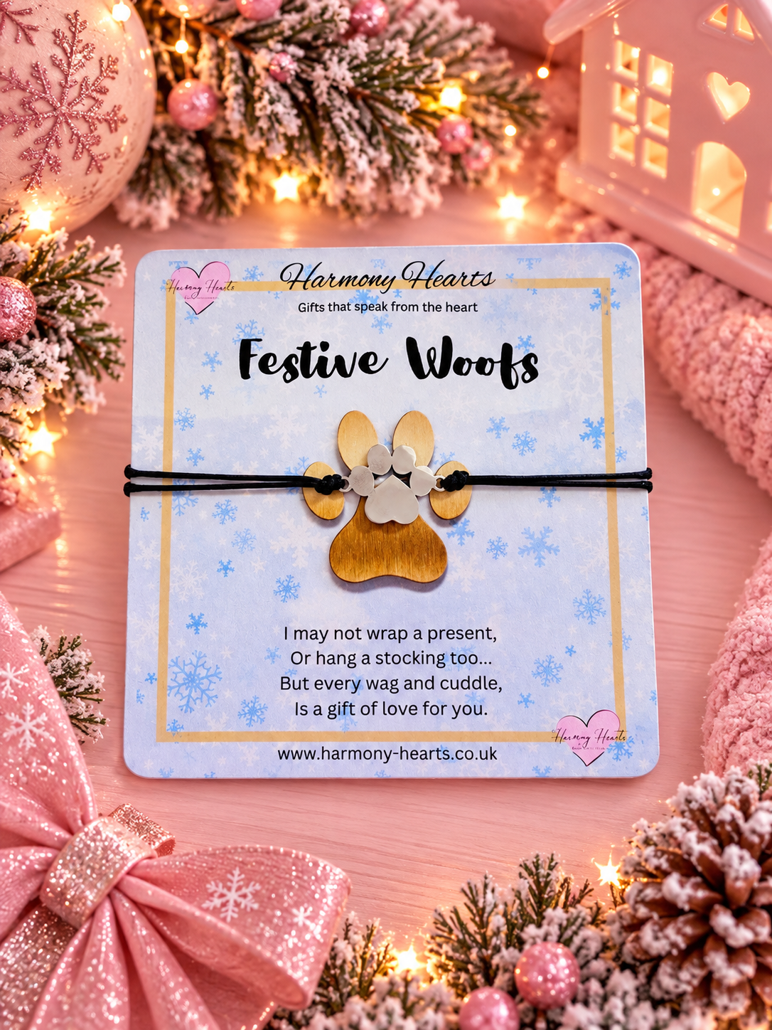 A festive dog-themed gift card from Harmony Hearts featuring a gold paw-shaped bracelet on a black cord, displayed on a decorated Christmas background with lights, ornaments, and pink bows.