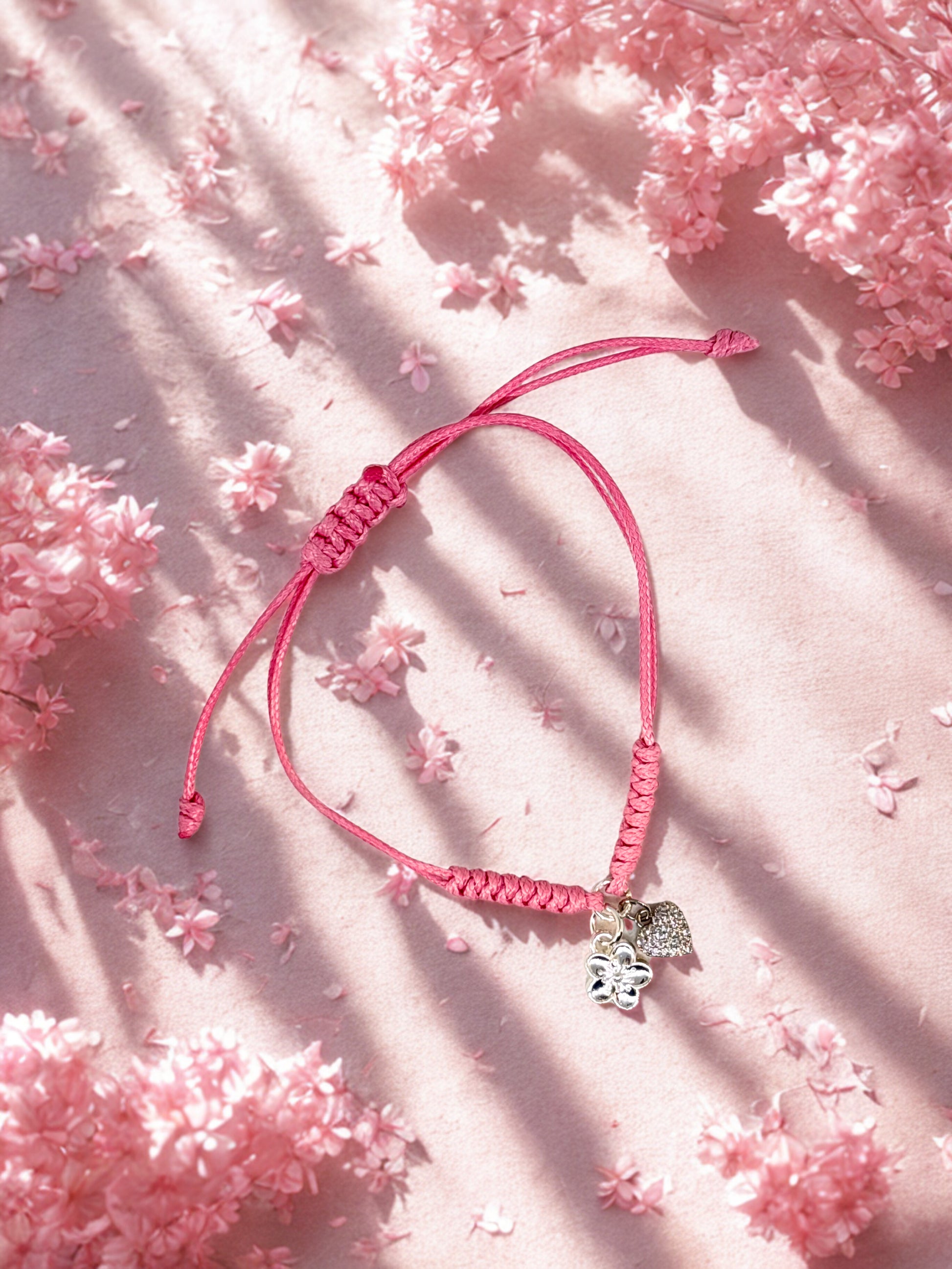 Pink braided bracelet with a heart and flower charm on a pink floral background