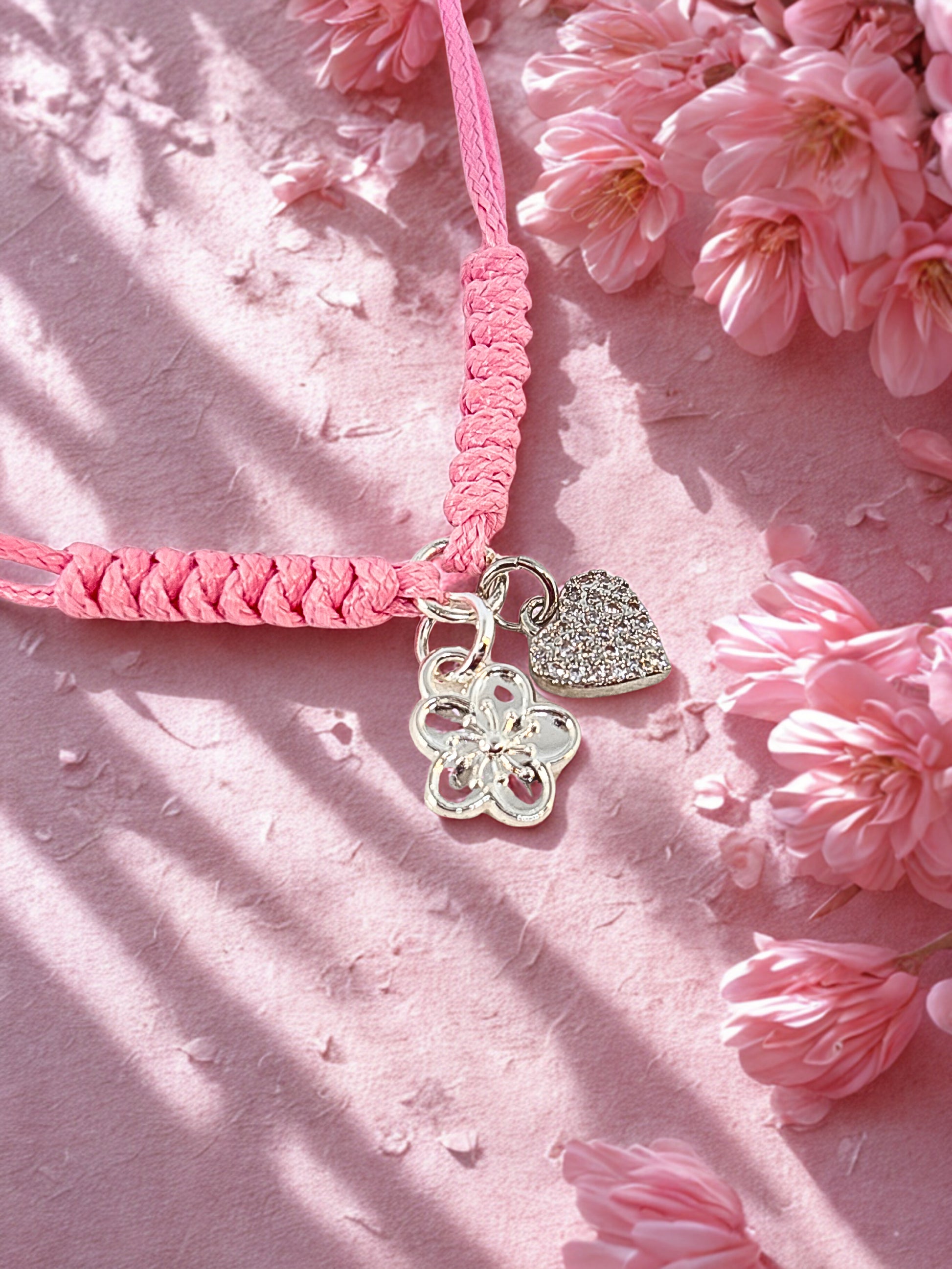 Pink braided bracelet with silver charms on a pink floral background