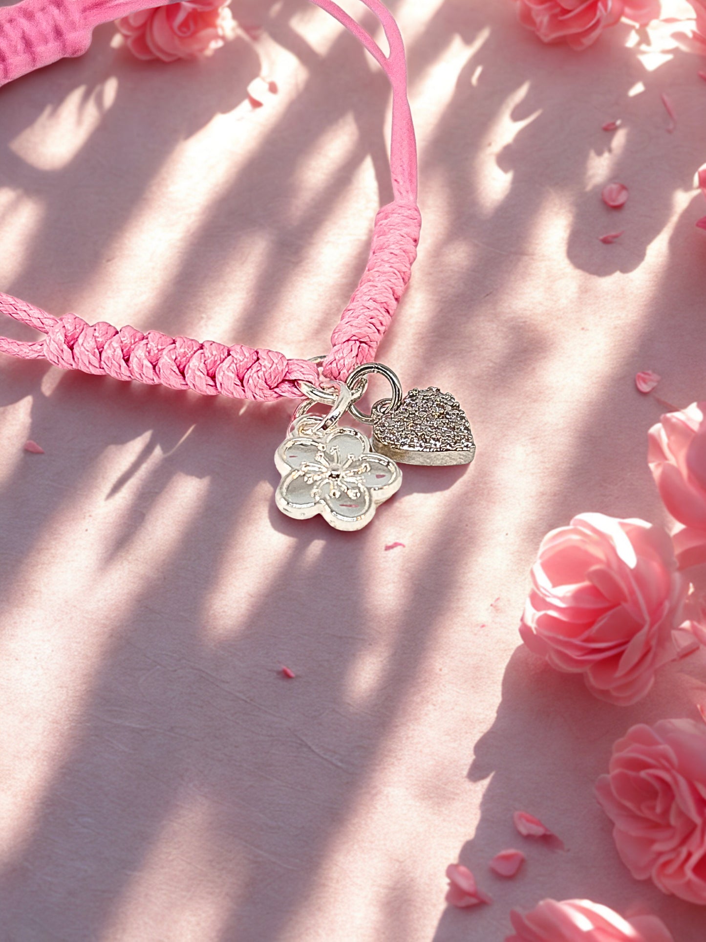 Pink braided bracelet with silver charms on a pink floral background