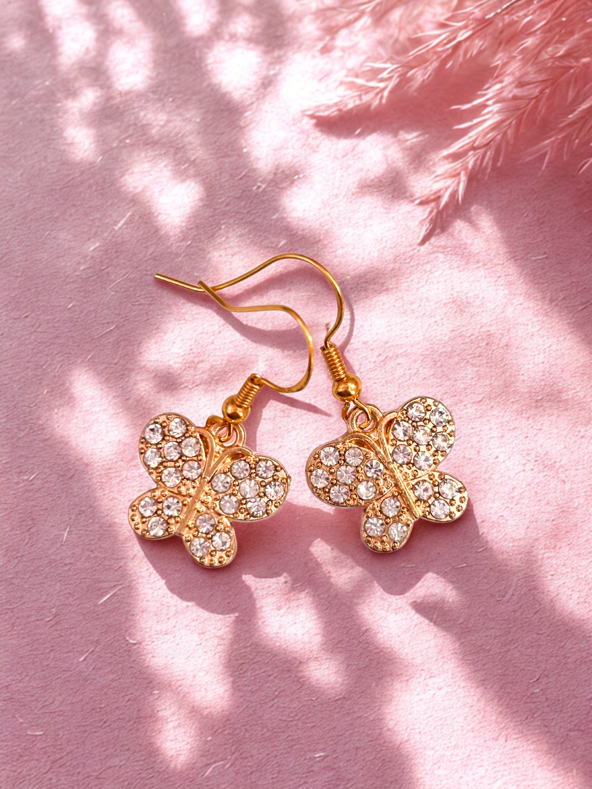 Gold sparkly butterfly earrings on a pink background