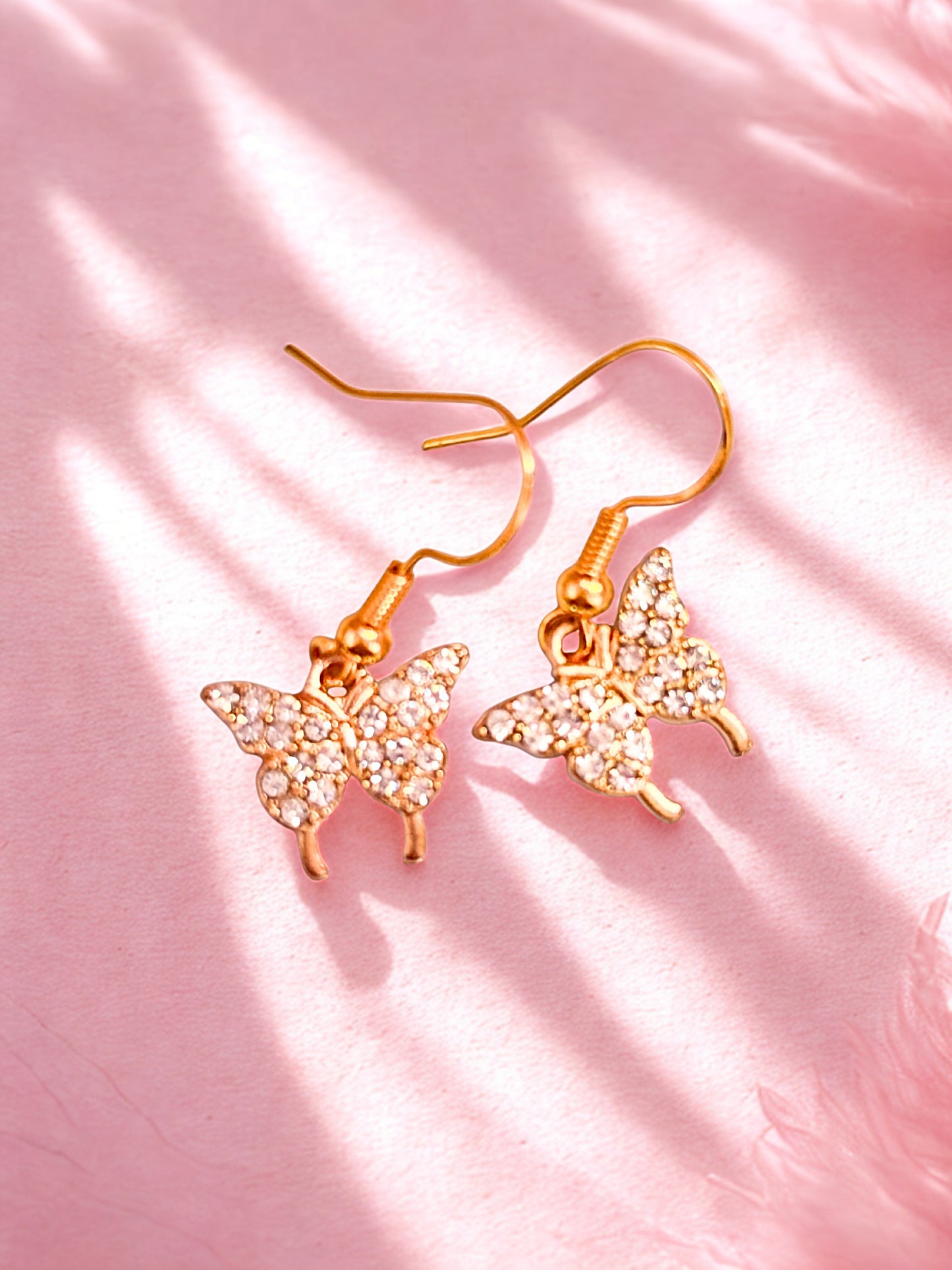 Butterfly-shaped earrings with gold and crystal details on a pink background
