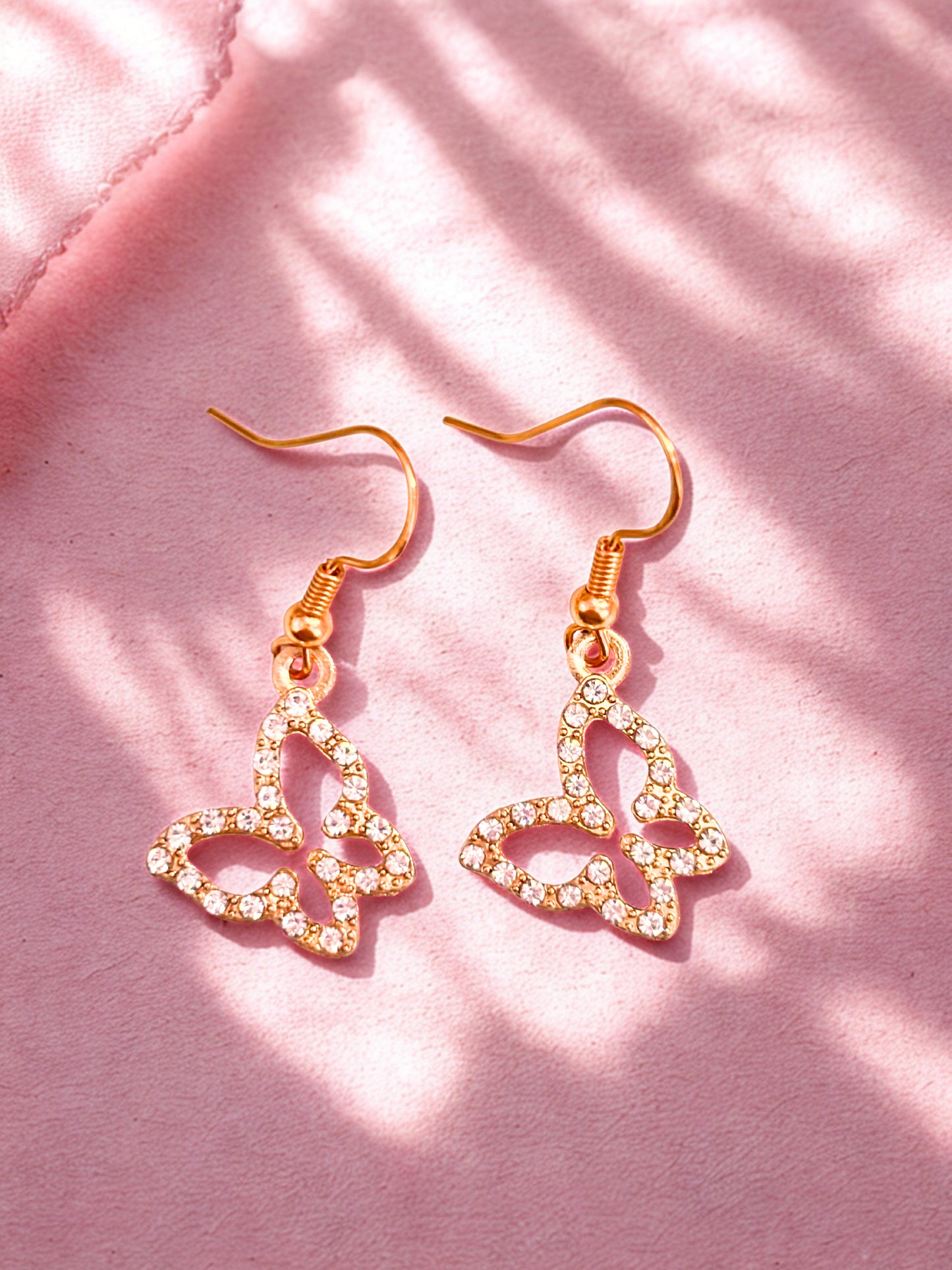 Heart-shaped earrings with gold and clear stones on a pink background