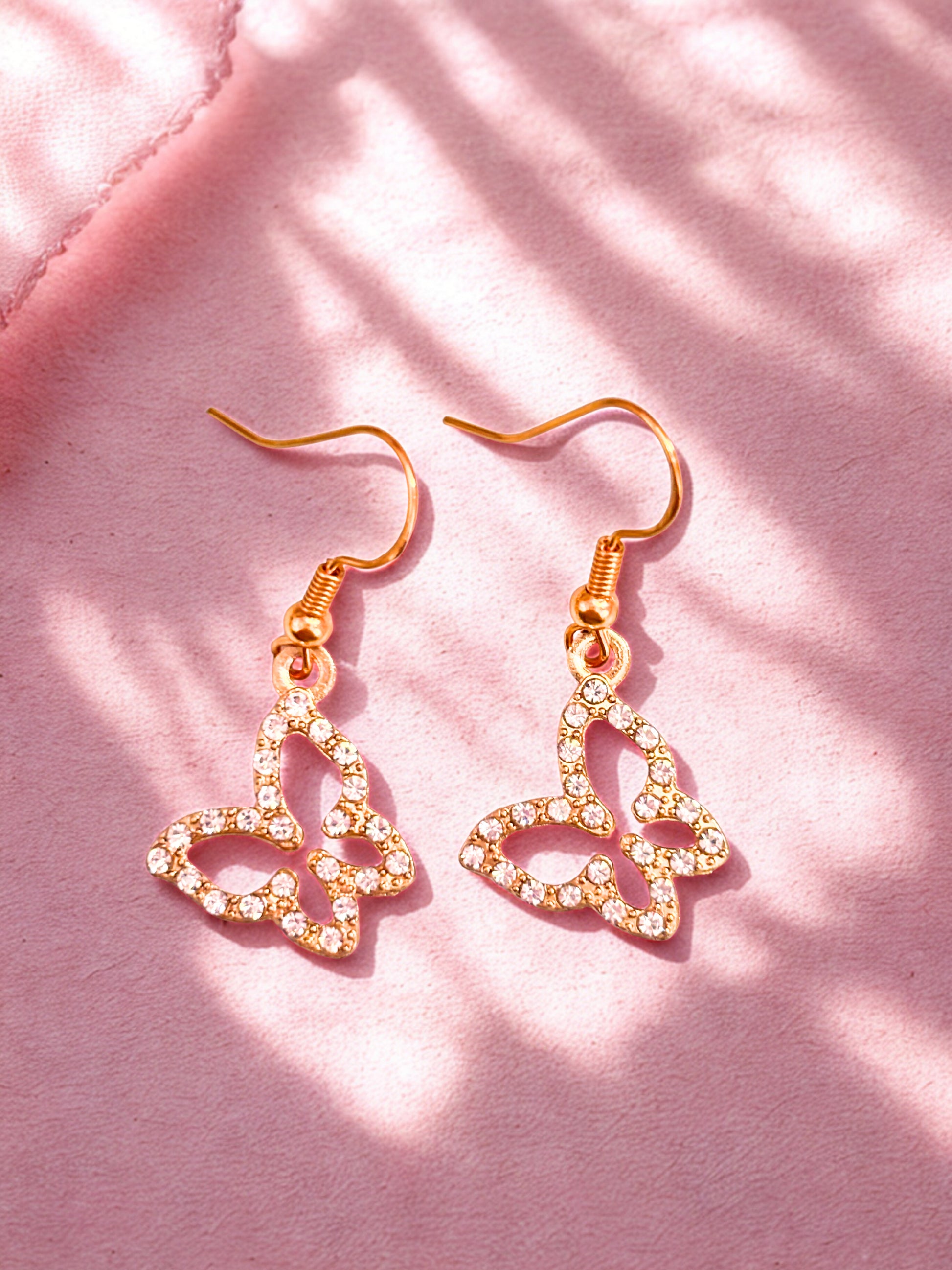 Heart-shaped earrings with gold and clear stones on a pink background