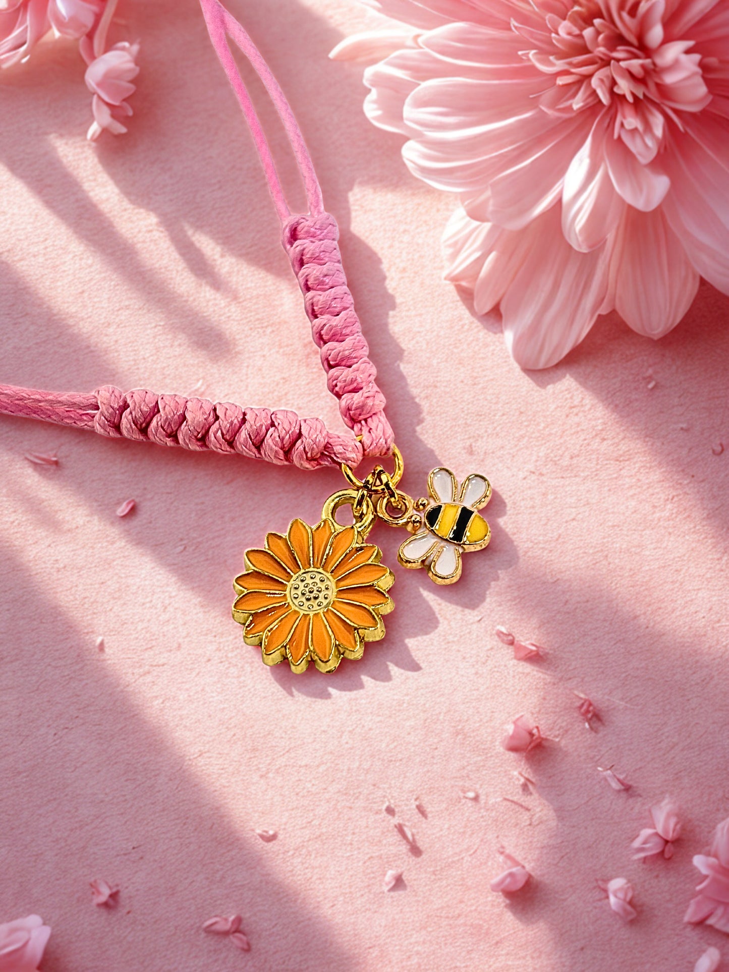 Pink braided bracelet with sunflower and bee charms on a pink floral background