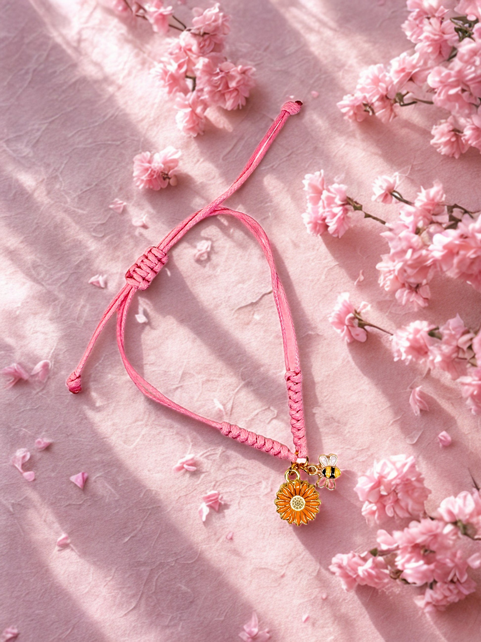 Pink bracelet with a sunflower and bee charm on a pink floral background