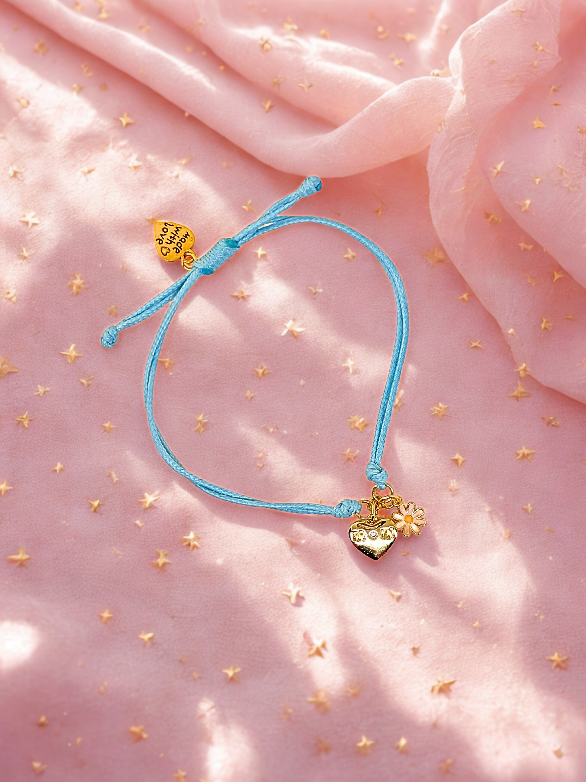 Blue bracelet with gold heart charms on a pink fabric background