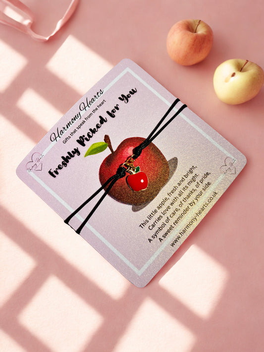 Black cord bracelet with apple charm on a pink poem card on a pink backgound