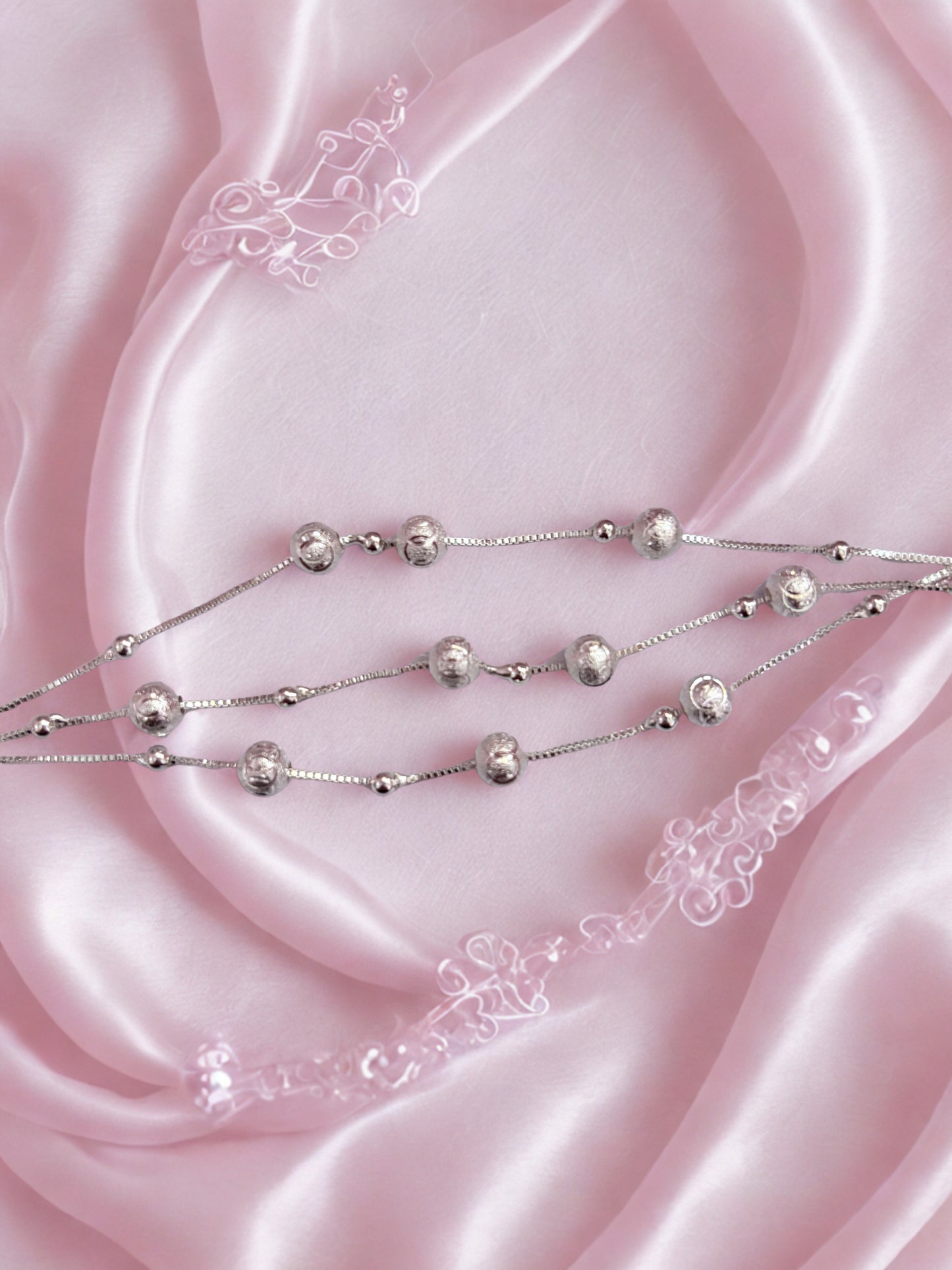 Silver beaded bracelet on pink satin fabric