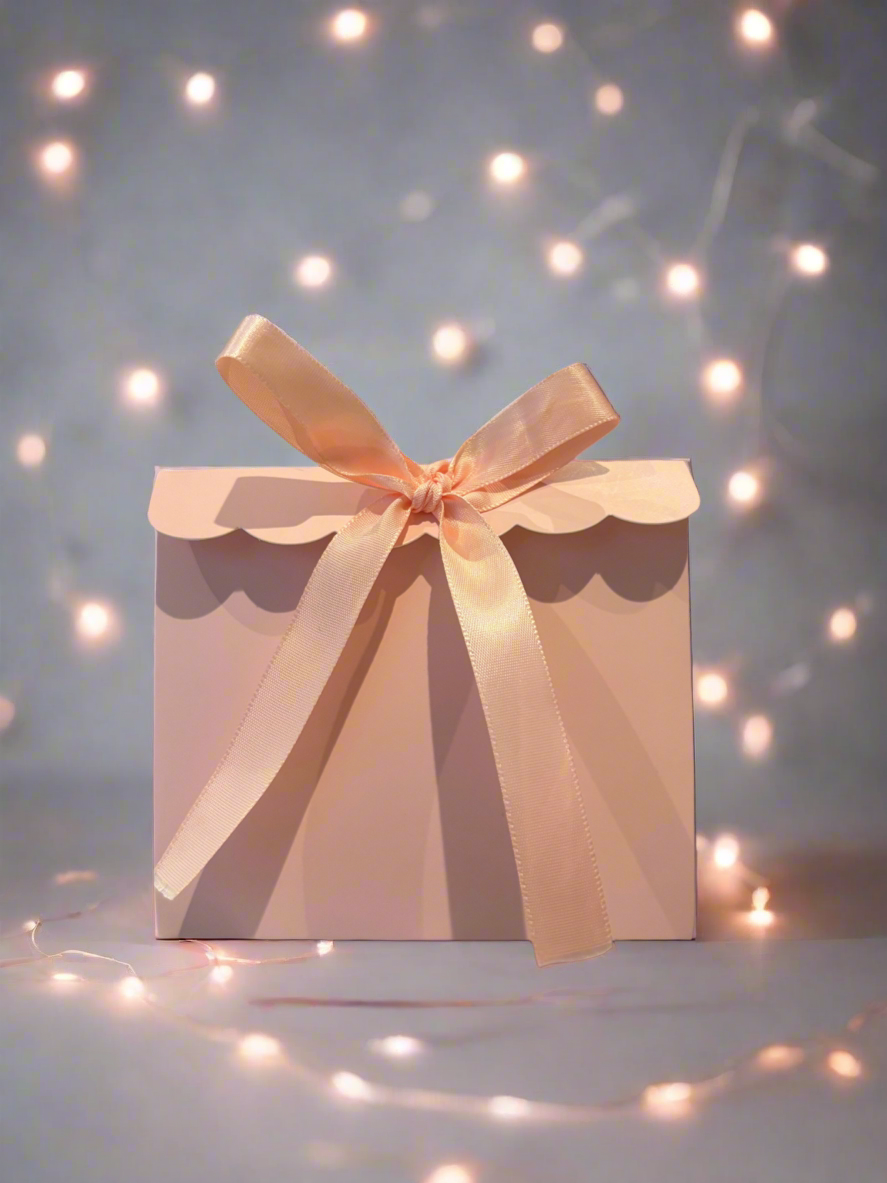 Gift box with a pink ribbon on a soft focus background with lights
