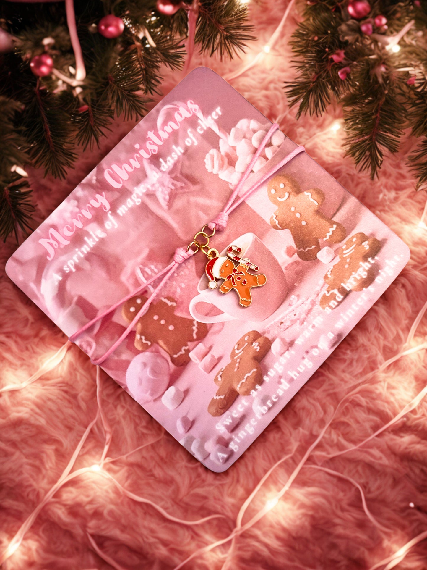Pink Christmas-themed card with gingerbread cookies and a pink bow  and a gingerbread man charm bracelet on a soft pink background with lights.