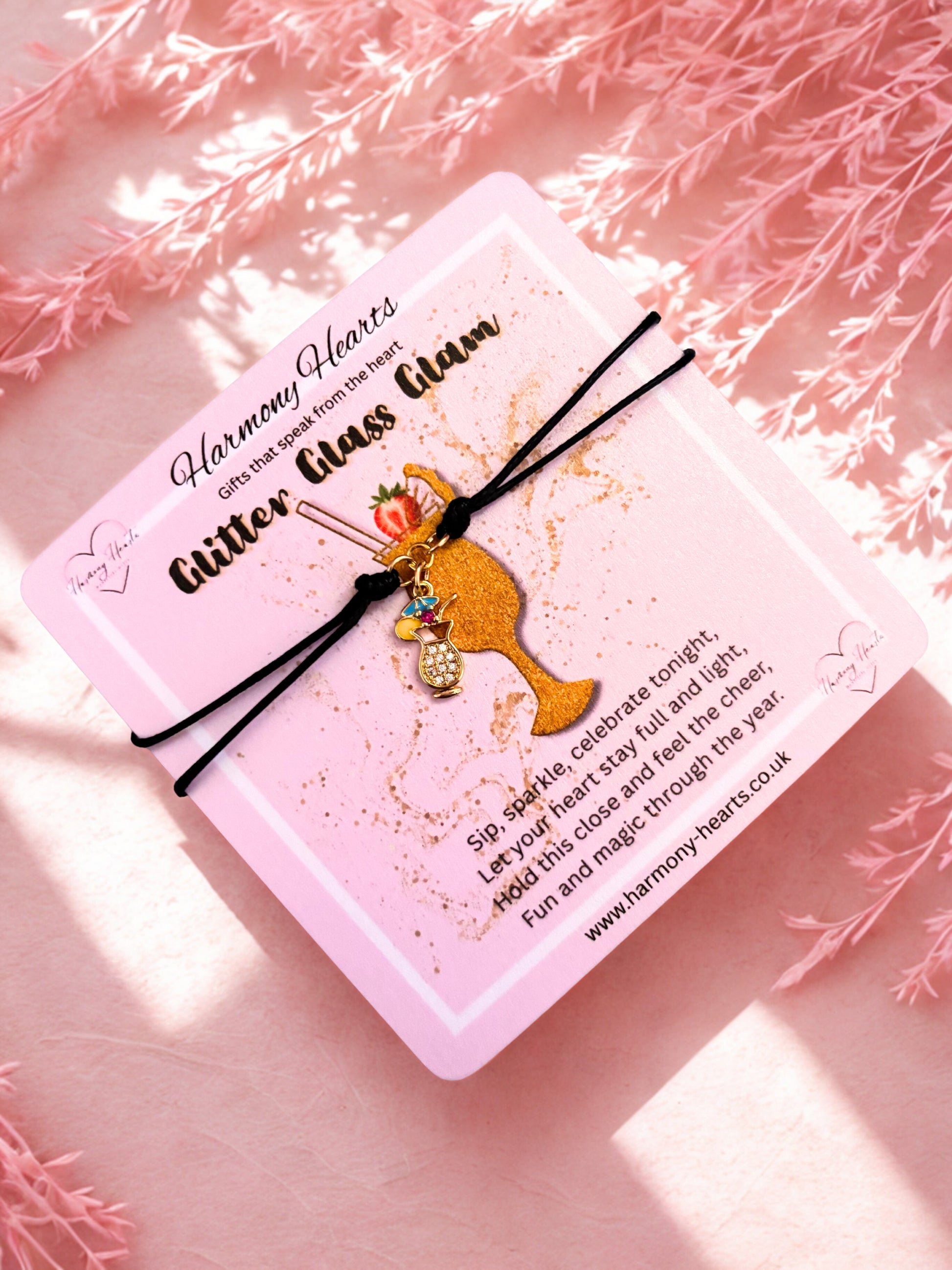 Bracelet with a gold cocktail charm on a pink card with text, against a soft pink background.
