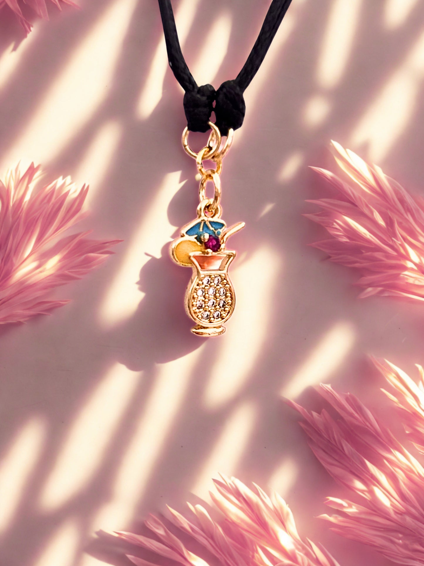 Gold cocktail glass charm with a colorful gem on a pink fluffy background
