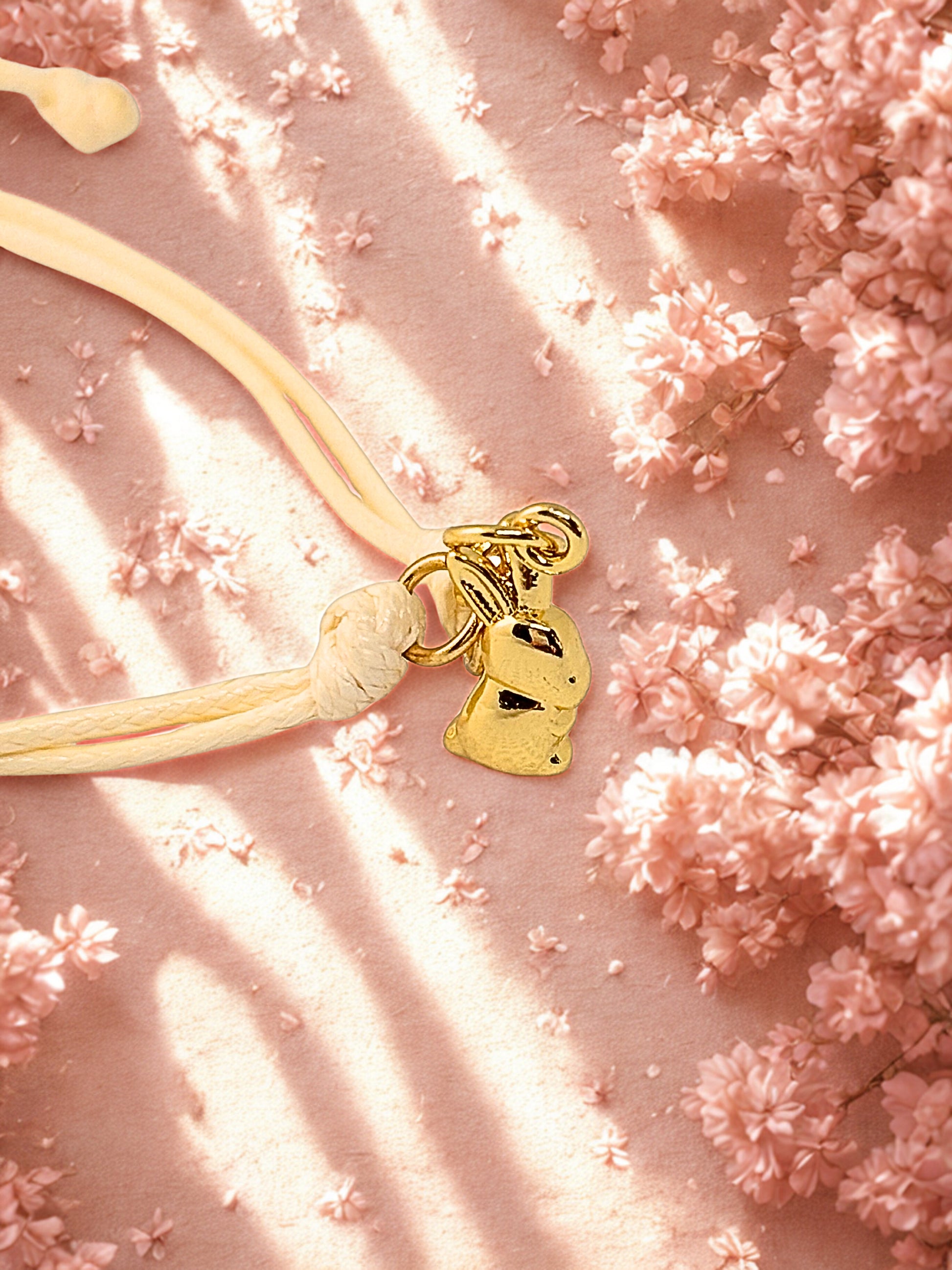 Gold bunny-shaped charm on a beige cord with pink floral background