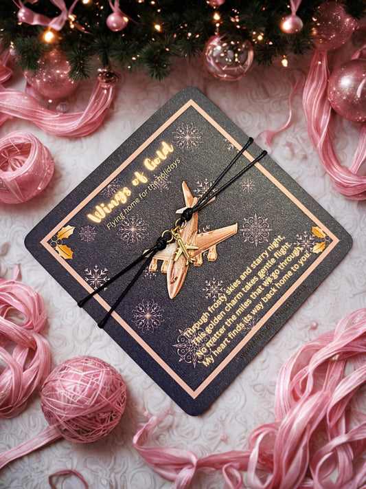 Bracelet with gold aeroplane charm on a decorative card with pink yarn balls and Christmas decorations.